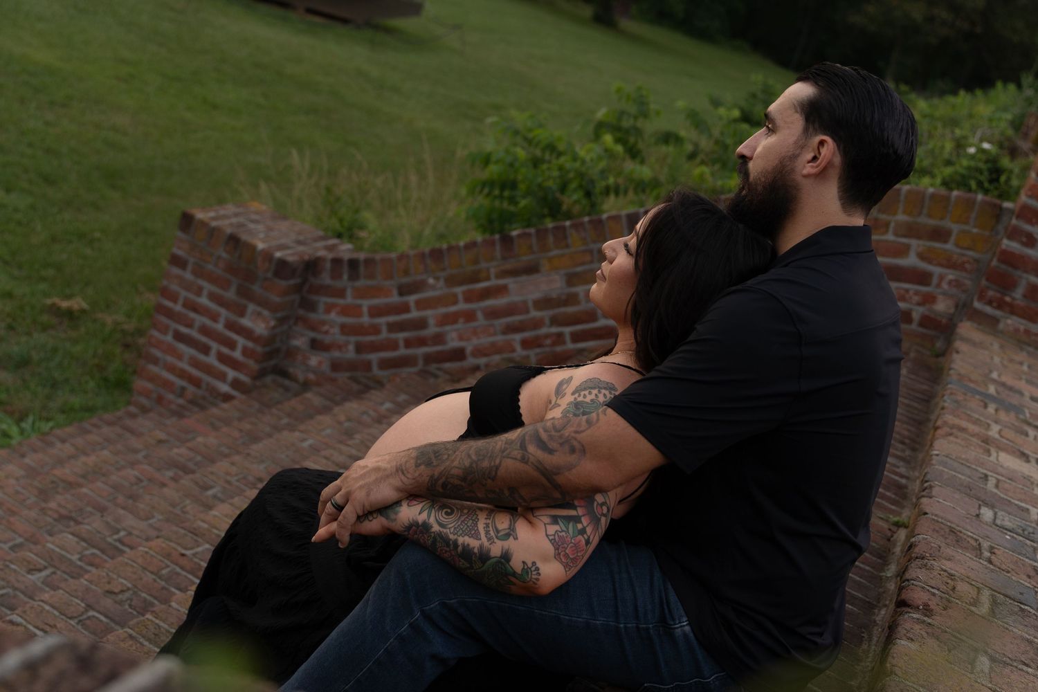 Tattooed couple sitting together on brick steps in an intimate outdoor portrait. Taken by Row And Co Photography in FXBG VA