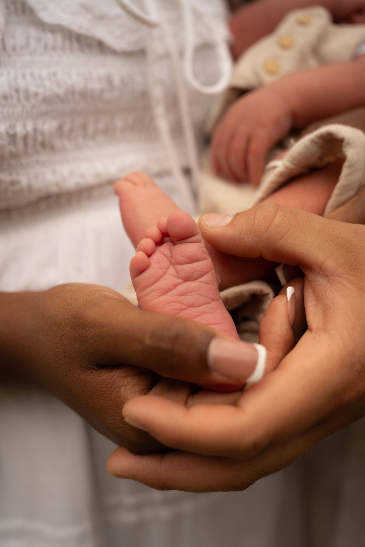 Adult hands gently cradling tiny newborn baby feet, showcasing a tender moment between parent and infant.