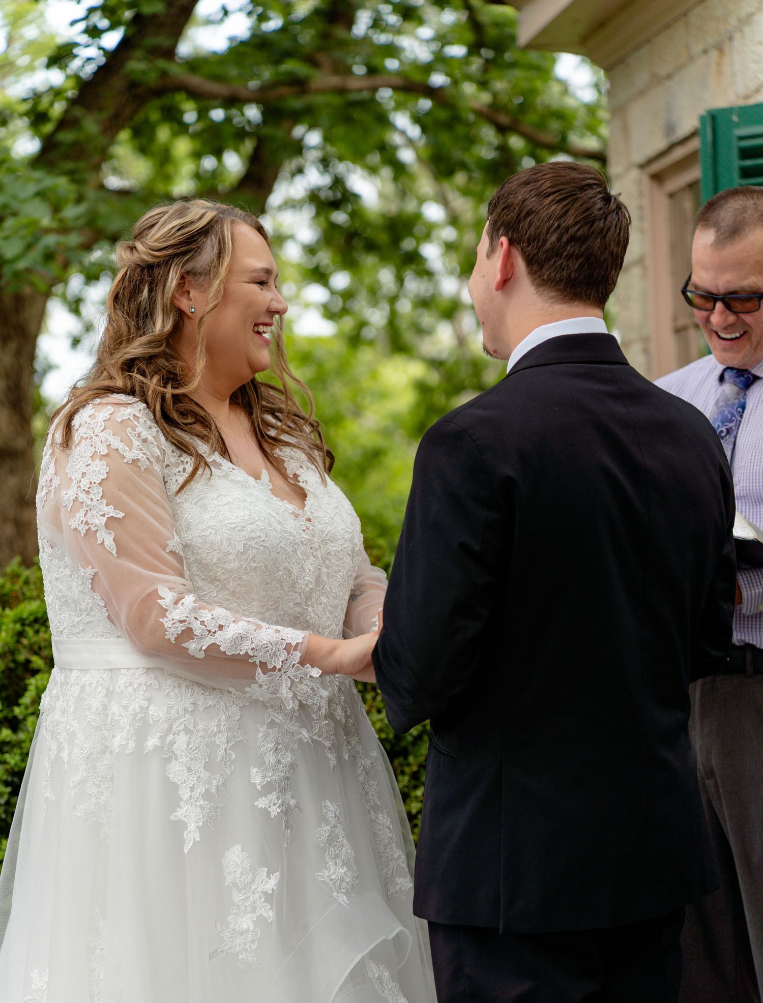 Bride in lace wedding gown smiling at groom during outdoor wedding ceremony. Taken by Row And Co Photography in FXBG VA