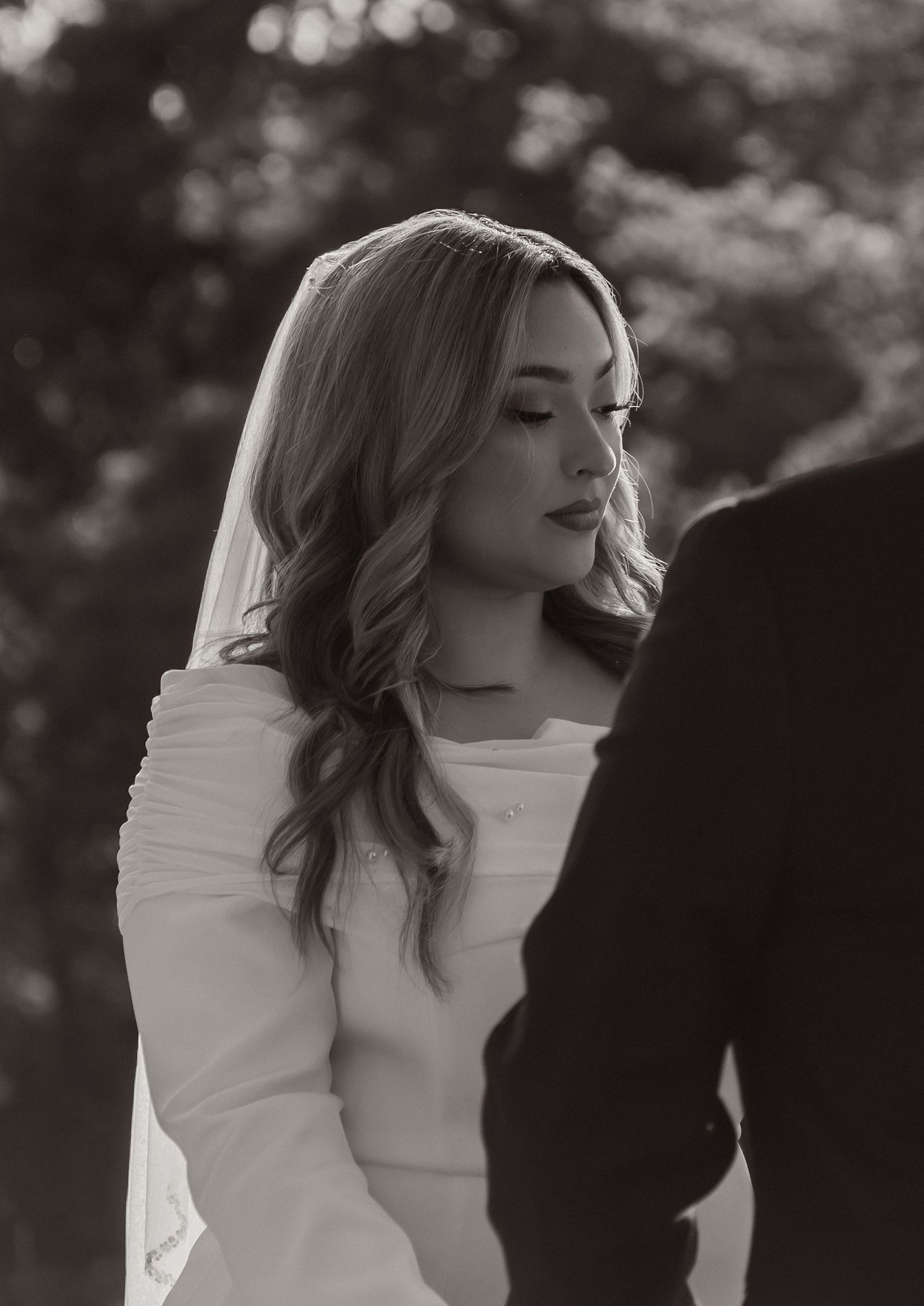 Black and white wedding photo of a bride in a white gown and veil, looking down with soft elegant makeup.