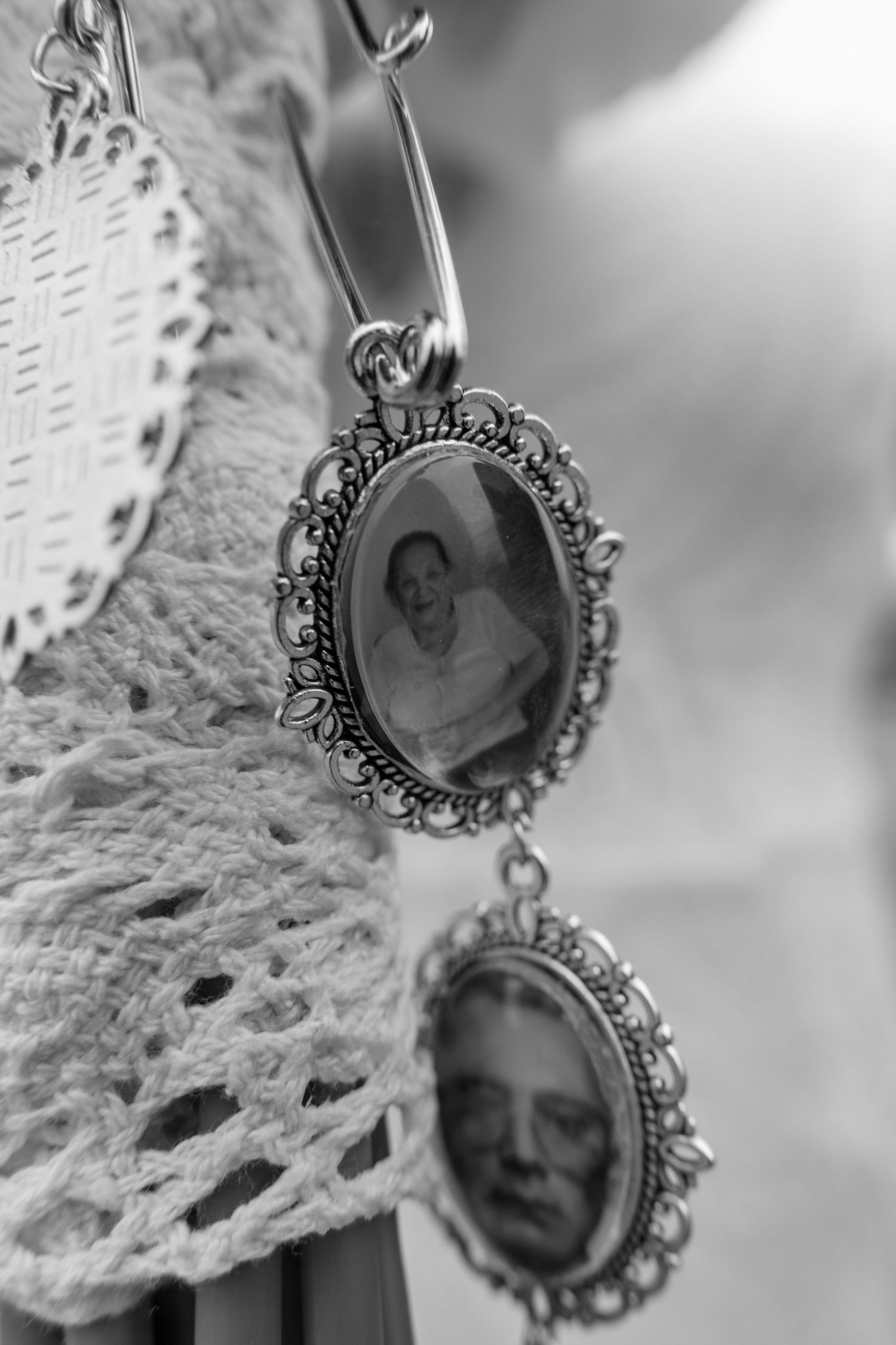Black and white photo of two ornate vintage oval locket charms with portrait photos hanging from a safety pin.