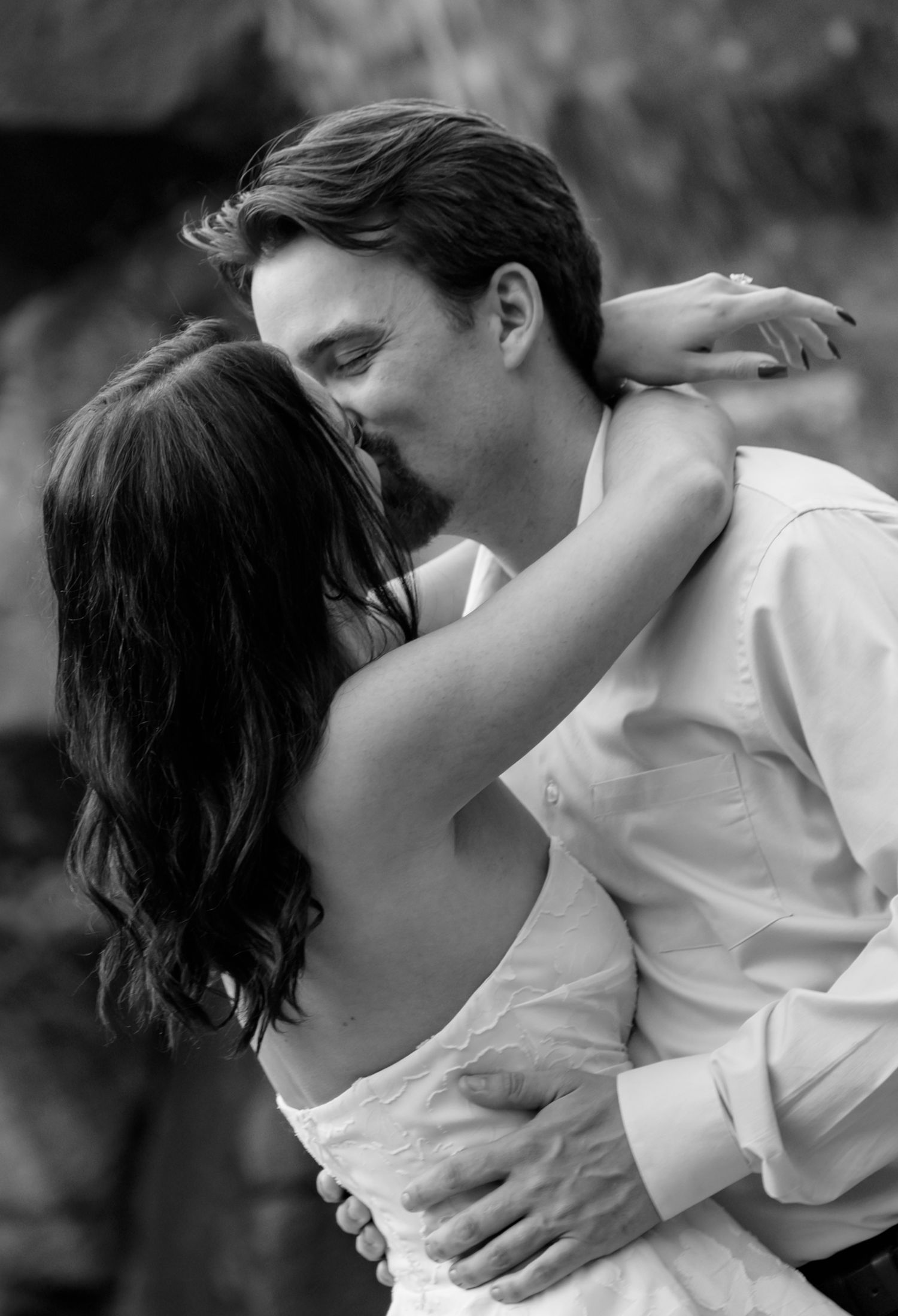 Black and white romantic photo of bride and groom sharing a tender kiss and embrace outdoors. Taken by Row And Co Photography in FXBG VA