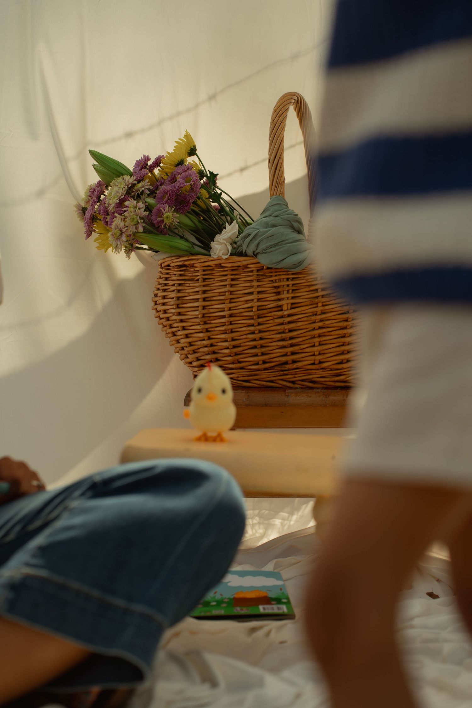 A wicker basket with colorful flowers sits on wooden steps beside a small duck toy, as children play nearby. Taken by Row And Co Photography