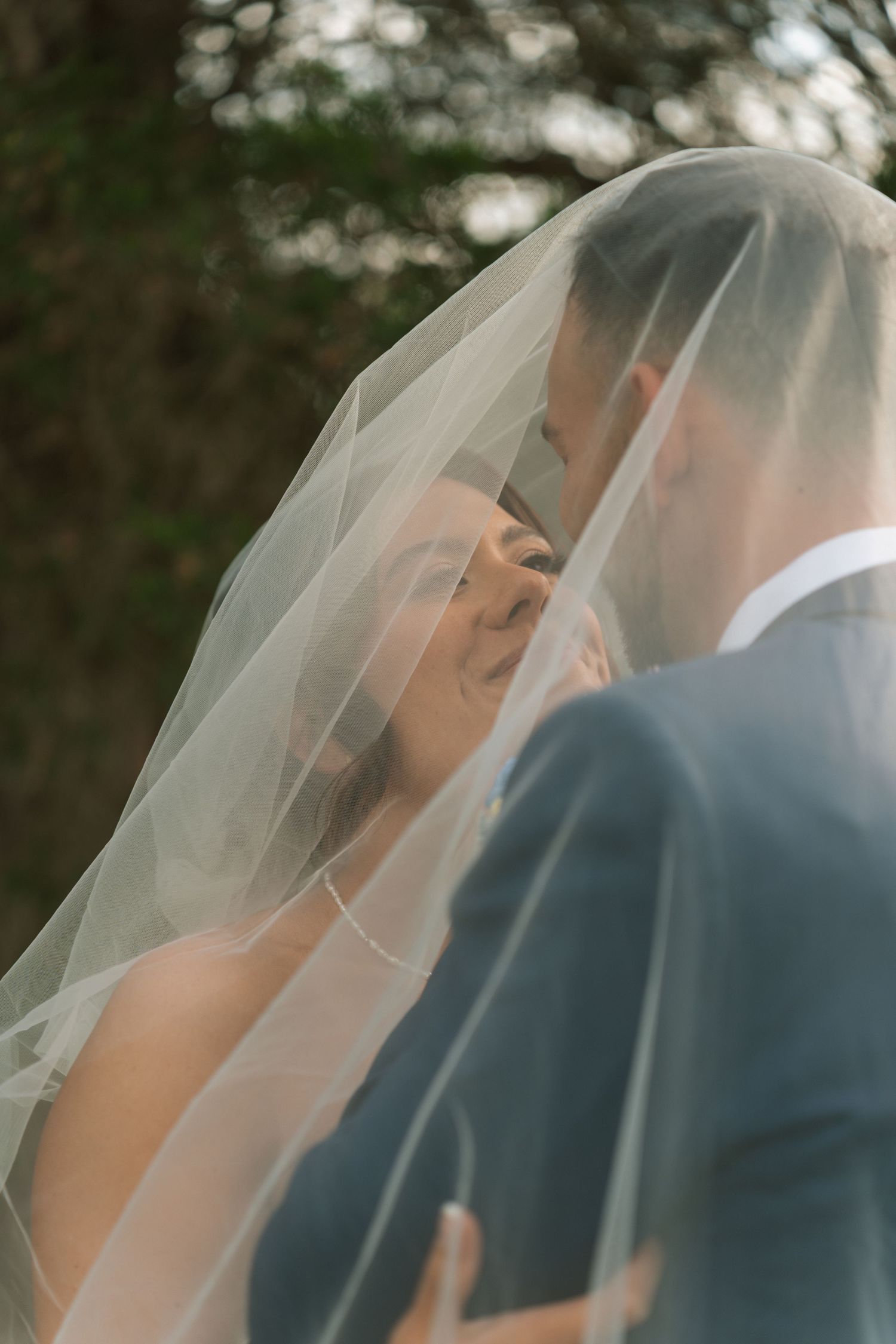 Bride and groom sharing a romantic moment under a flowing wedding veil outdoors.