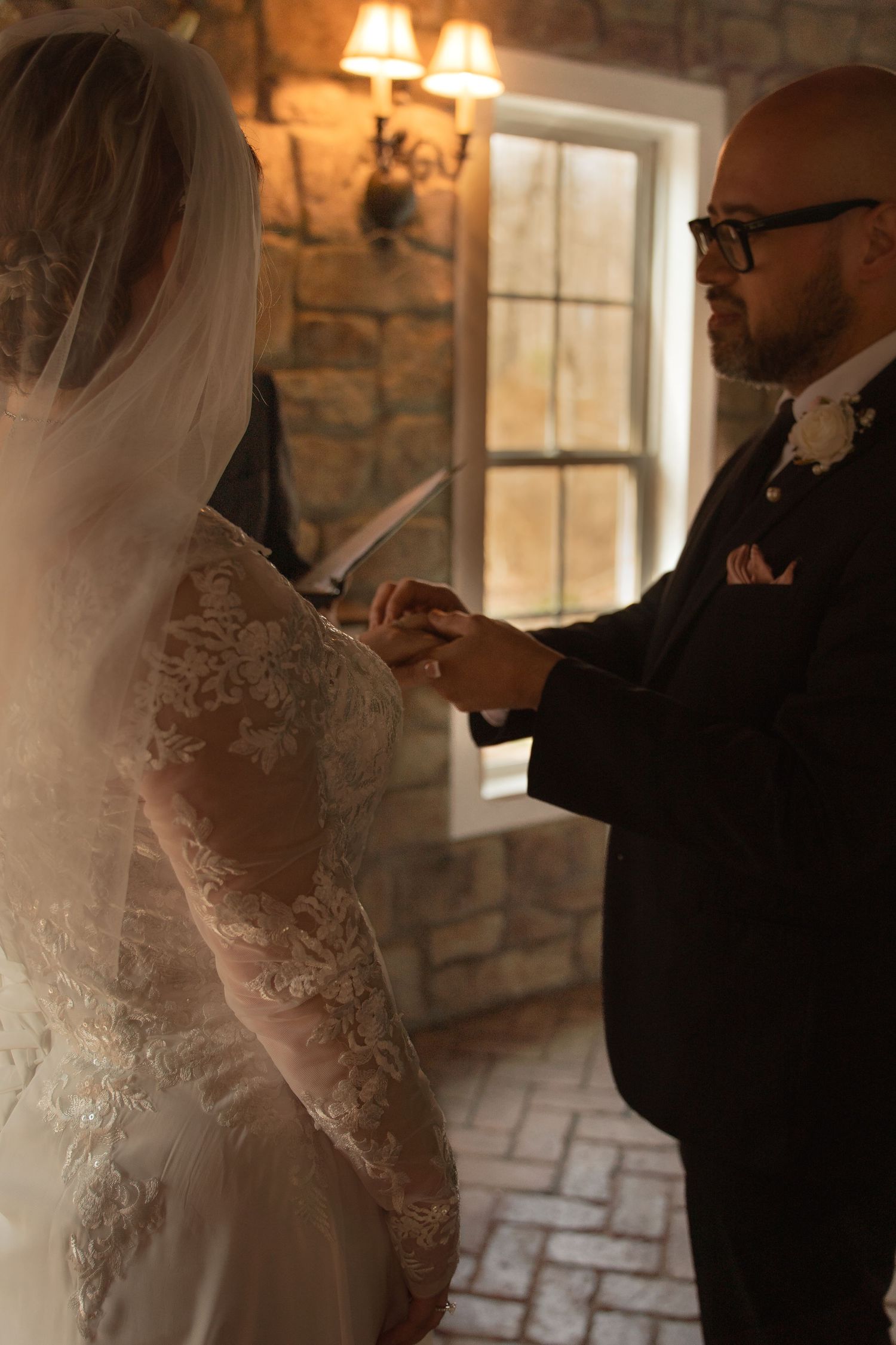 Bride and groom exchange rings during intimate wedding ceremony in rustic stone chapel with warm ambient lighting.