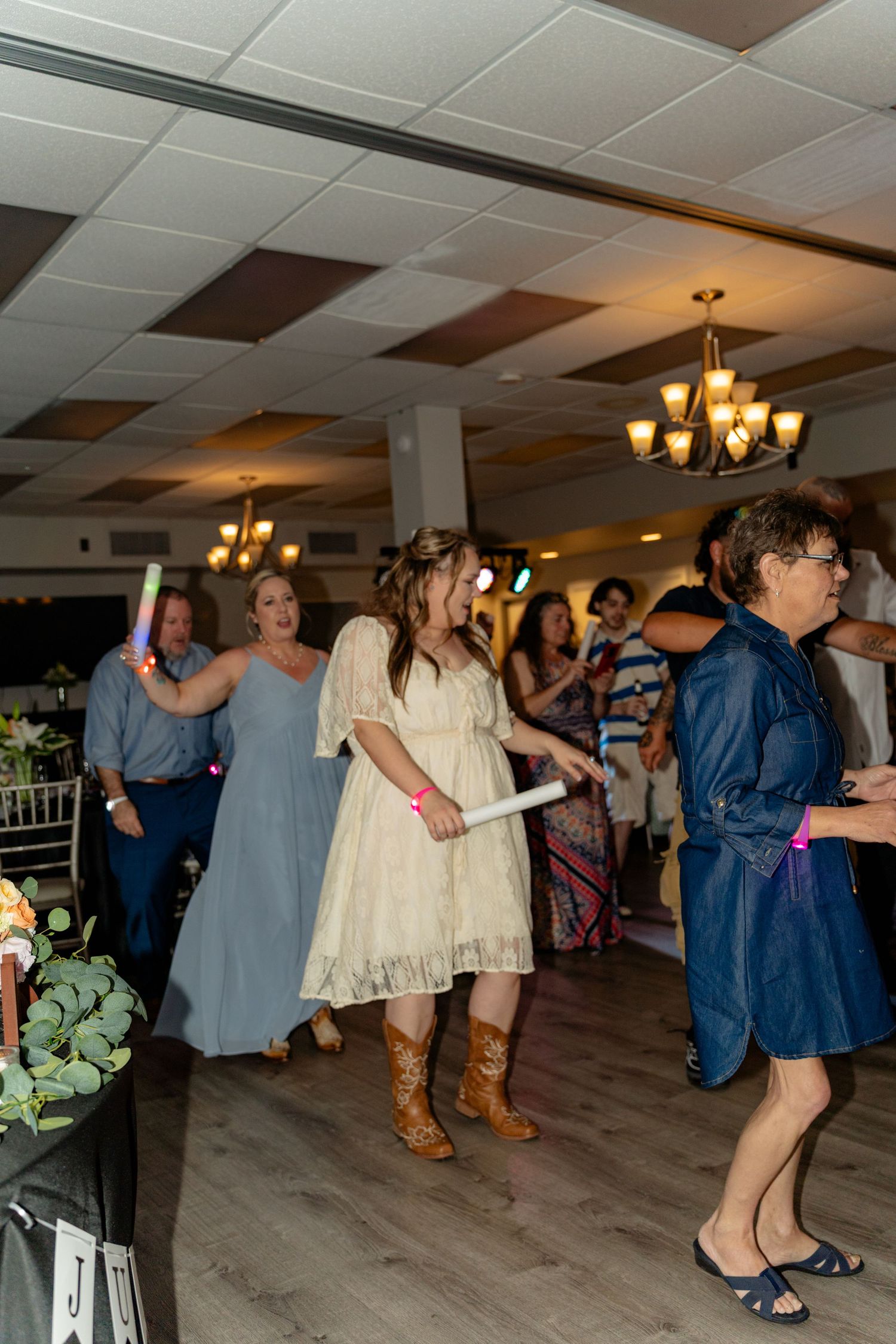 Guests dancing with glow sticks at a wedding reception in a decorated banquet hall.