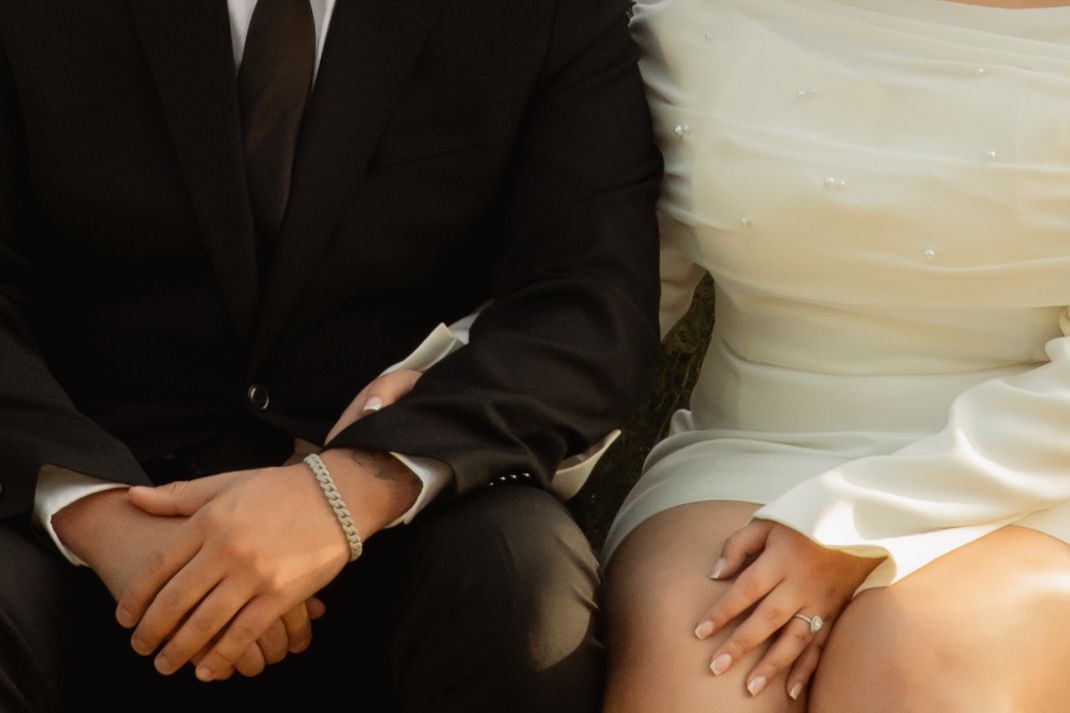 Close-up of bride and groom holding hands in wedding attire while seated. Taken by Row And Co Photography in FXBG VA