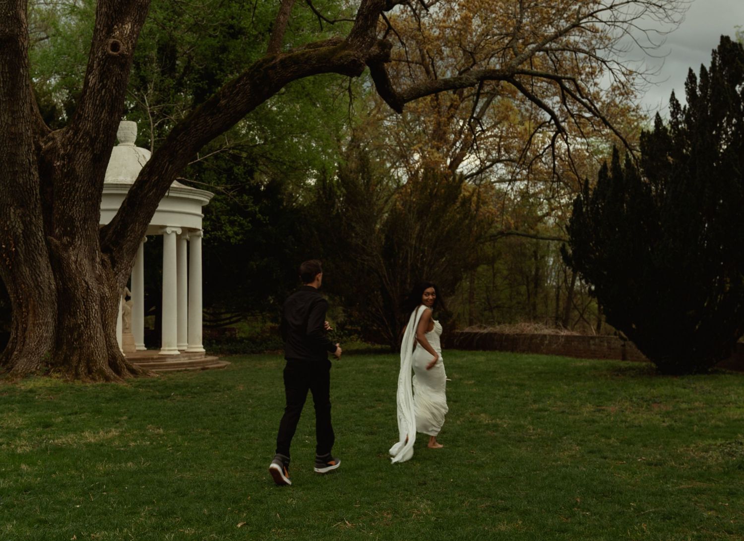 Bride in white gown and groom walking toward white columns in garden. Taken by Row And Co Photography in FXBG VA