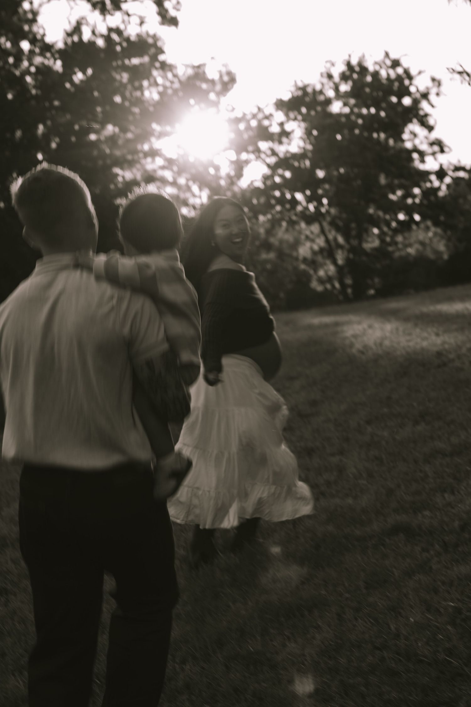 Black and white photo of a family walking outdoors at sunset, woman in white skirt smiling back at camera.