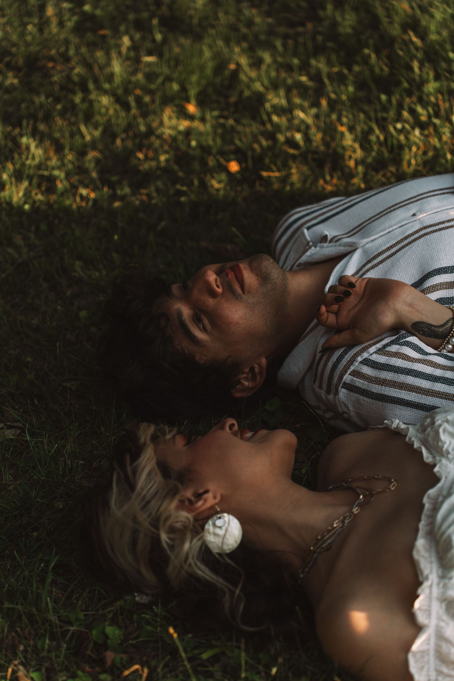 Romantic couple lying together on green grass in soft sunlight, sharing an intimate peaceful moment. Taken by Row And Co Photography in FXBG