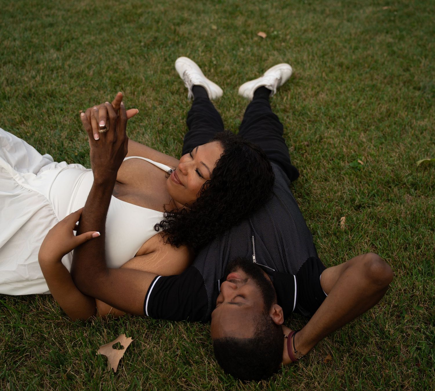 A couple in wedding attire lying on green grass, sharing a romantic moment outdoors.