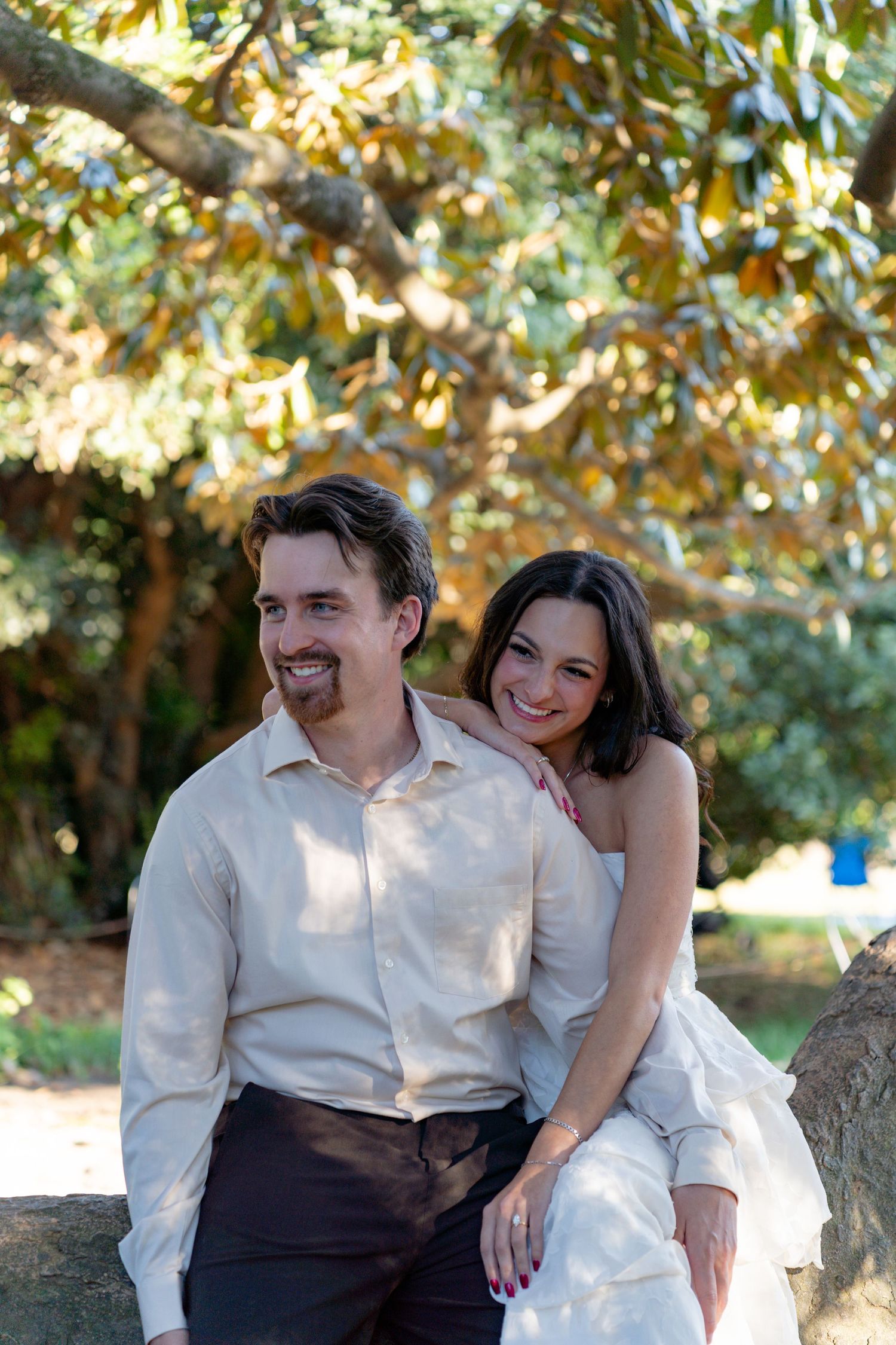 Smiling bride and groom sitting together under magnolia tree during outdoor wedding portrait session. Taken by Row And Co Photography
