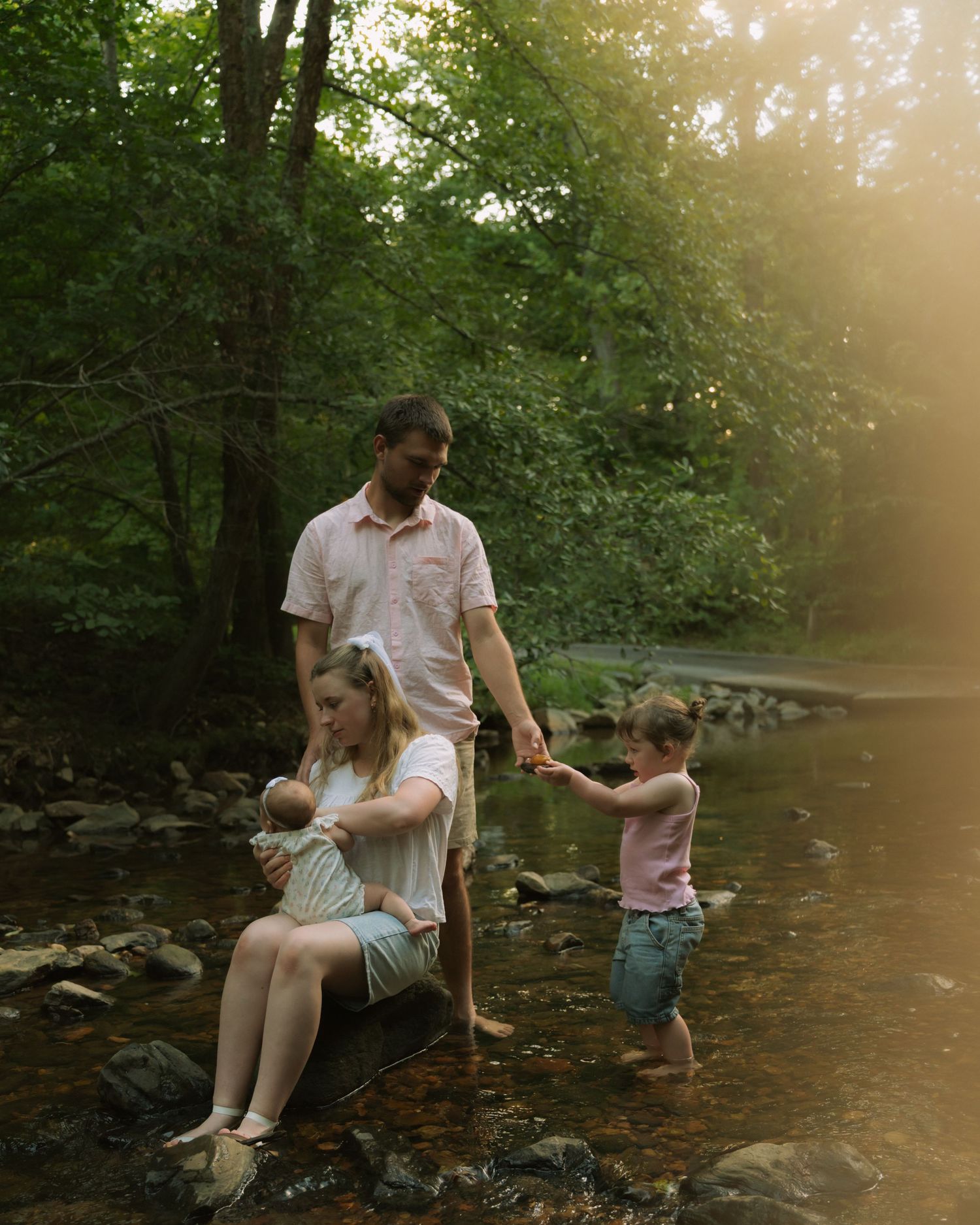 Family of four enjoying a peaceful creek in a lush forest, with golden hour light filtering through the trees.