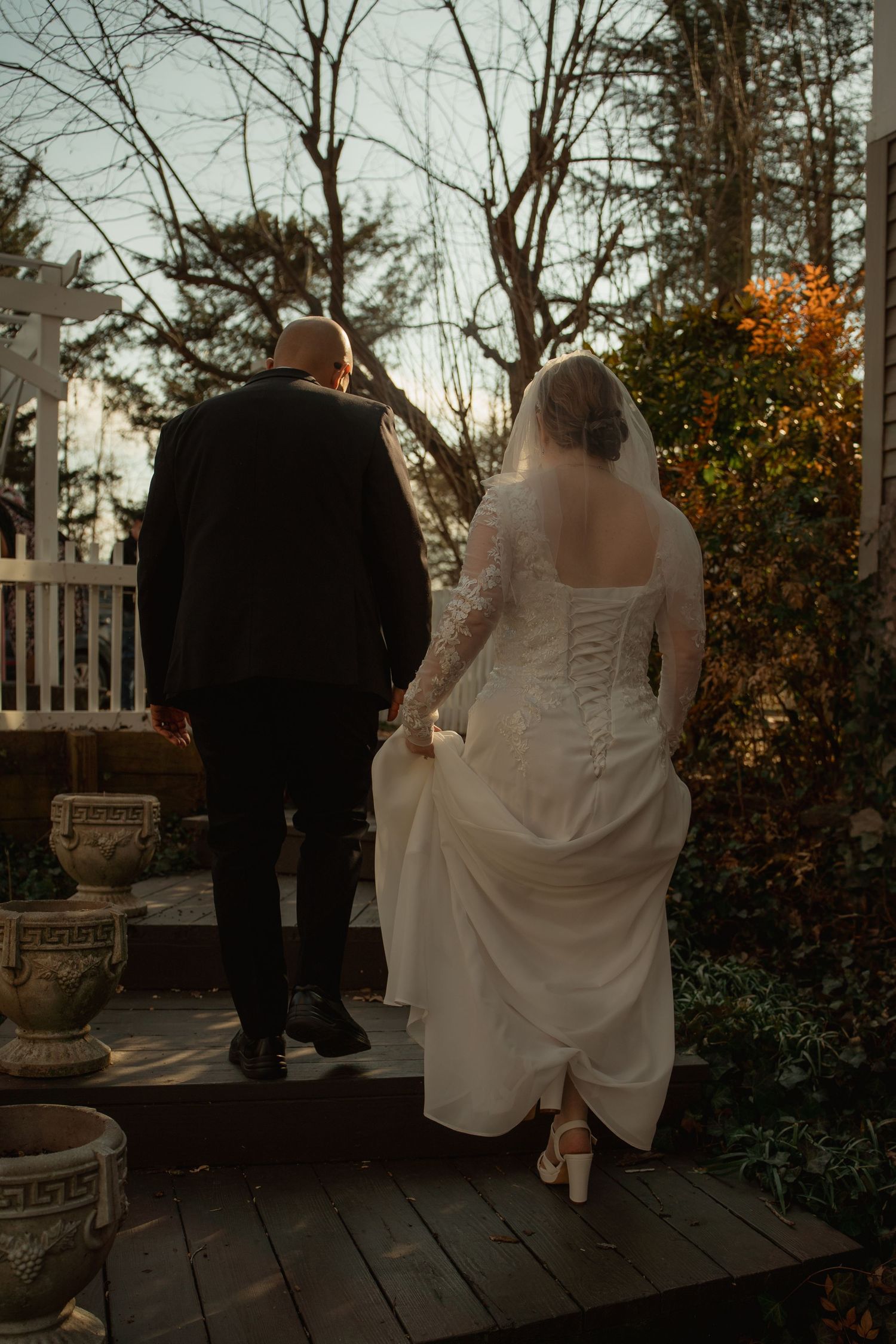 Bride and groom walking hand-in-hand on a wooden deck surrounded by autumn trees during an outdoor wedding ceremony.