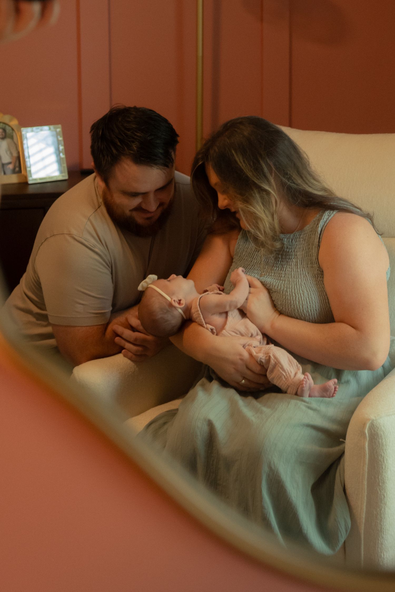 New parents lovingly gaze at their newborn baby while sitting in a cozy nursery chair.