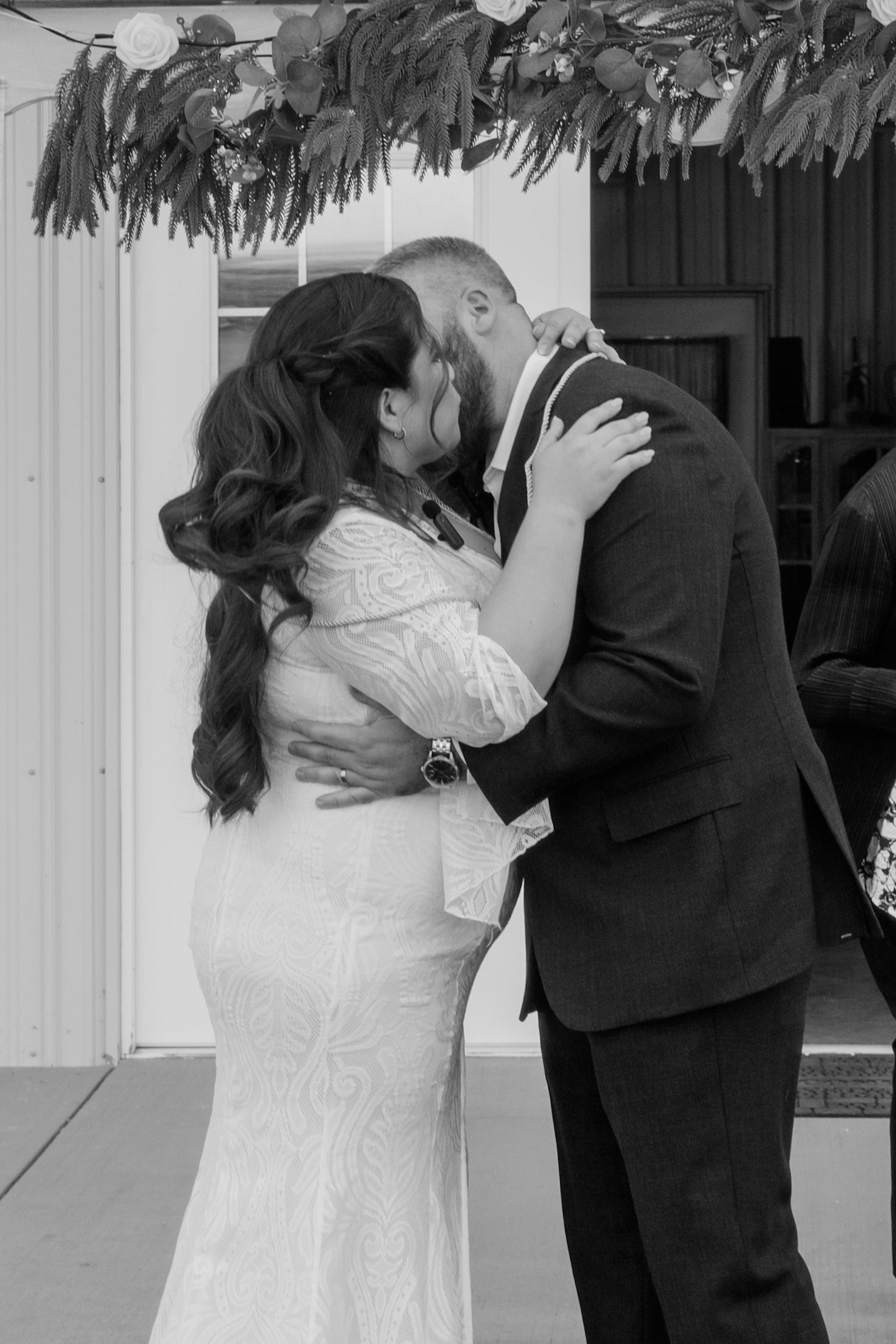 Black and white photo of a bride and groom sharing their first kiss at a wedding ceremony outdoors.
