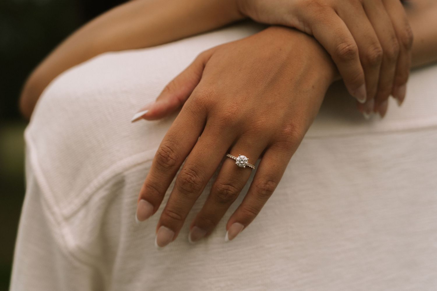 Close-up of a woman's hand wearing a solitaire diamond engagement ring, resting on a man's white shirt.