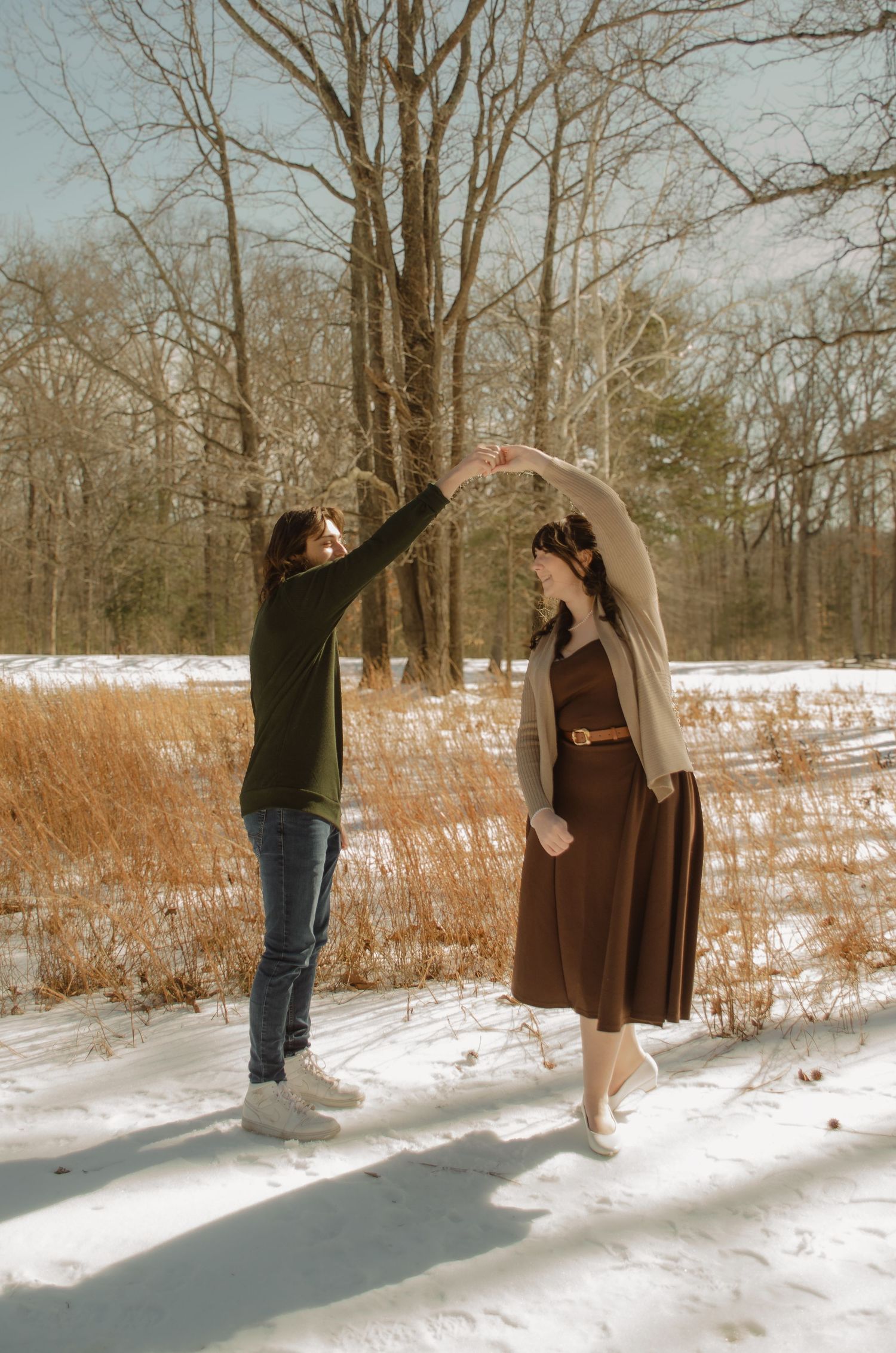 Couple dancing together in a snowy winter landscape surrounded by bare trees and golden grass. Taken by Row And Co Photography in FXBG VA