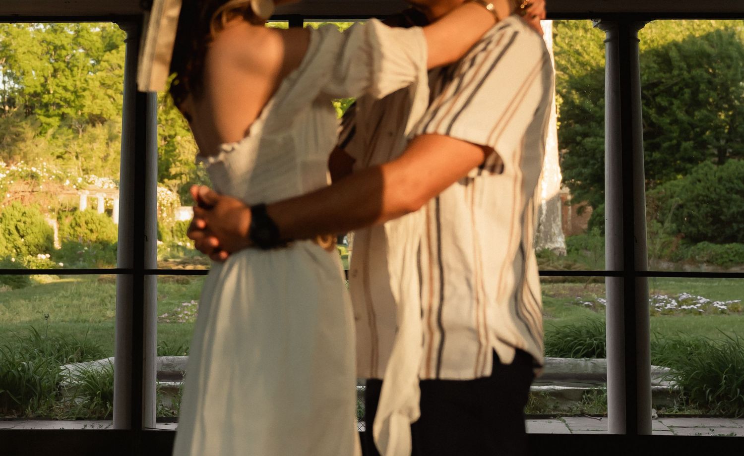 Couple embracing and dancing near large windows with garden views at sunset. Taken by Row And Co Photography in FXBG VA
