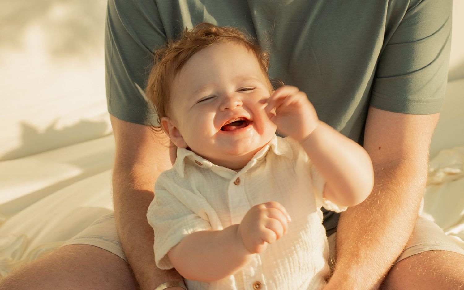 Happy red-haired baby laughing joyfully while sitting in parent's lap in warm sunlight. Taken by Row And Co Photography in FXBG VA