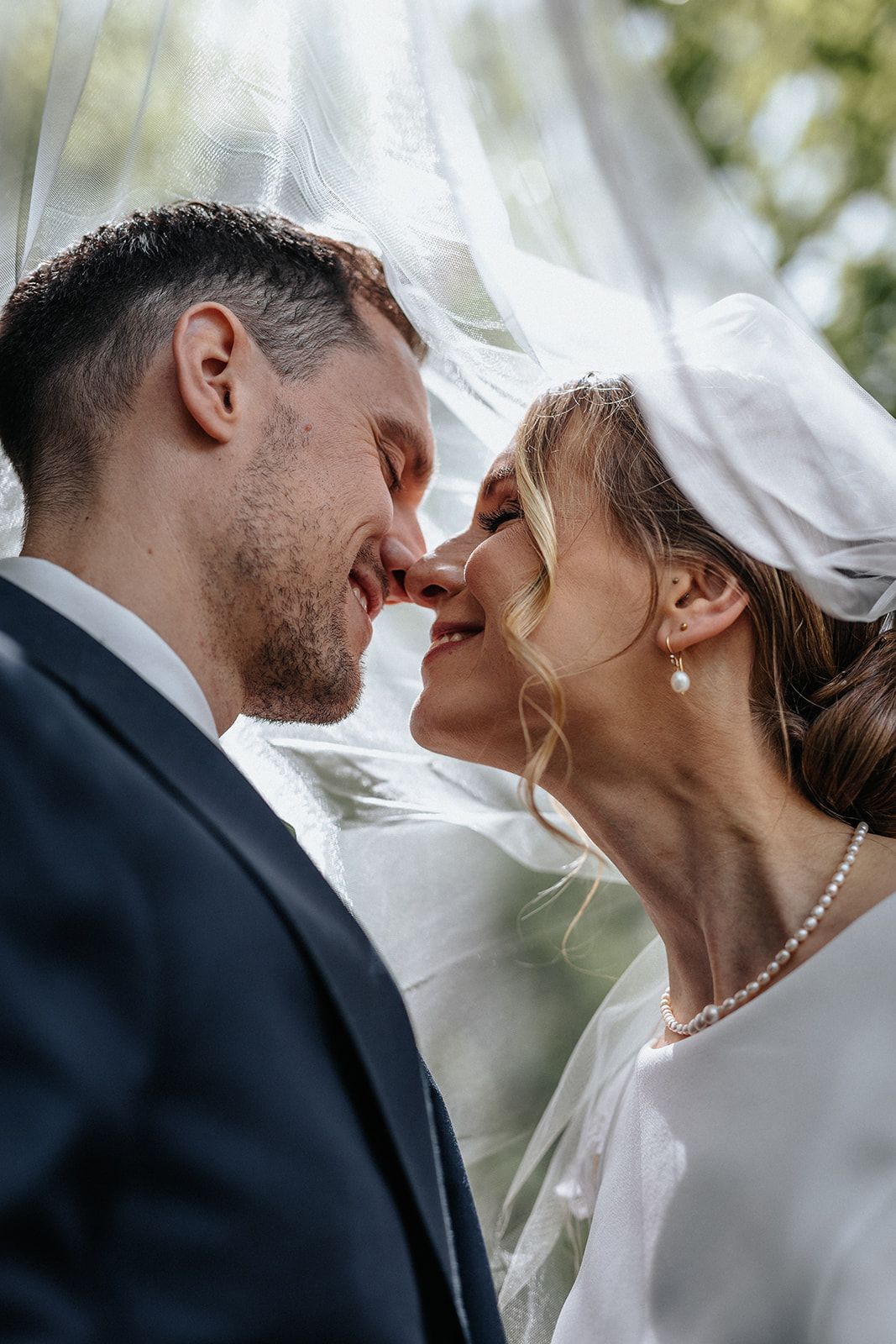 Close-up view of a bride and groom sharing an intimate moment under a delicate white veil outdoors.