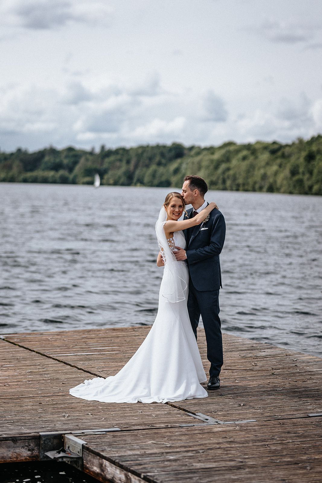 A couple shares a romantic moment on a wooden dock overlooking a serene lake on their wedding day.