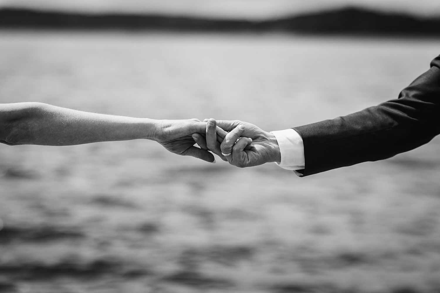A black and white close-up of two hands reaching towards each other against a blurred background.