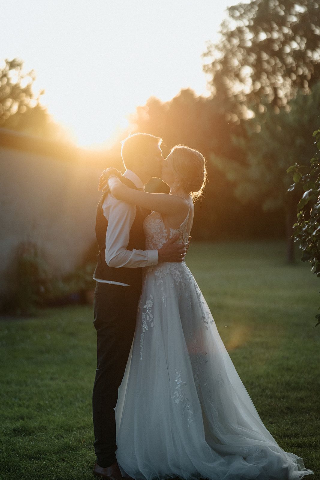 A romantic silhouette of a couple embracing during golden hour sunset in a garden setting with soft backlighting.