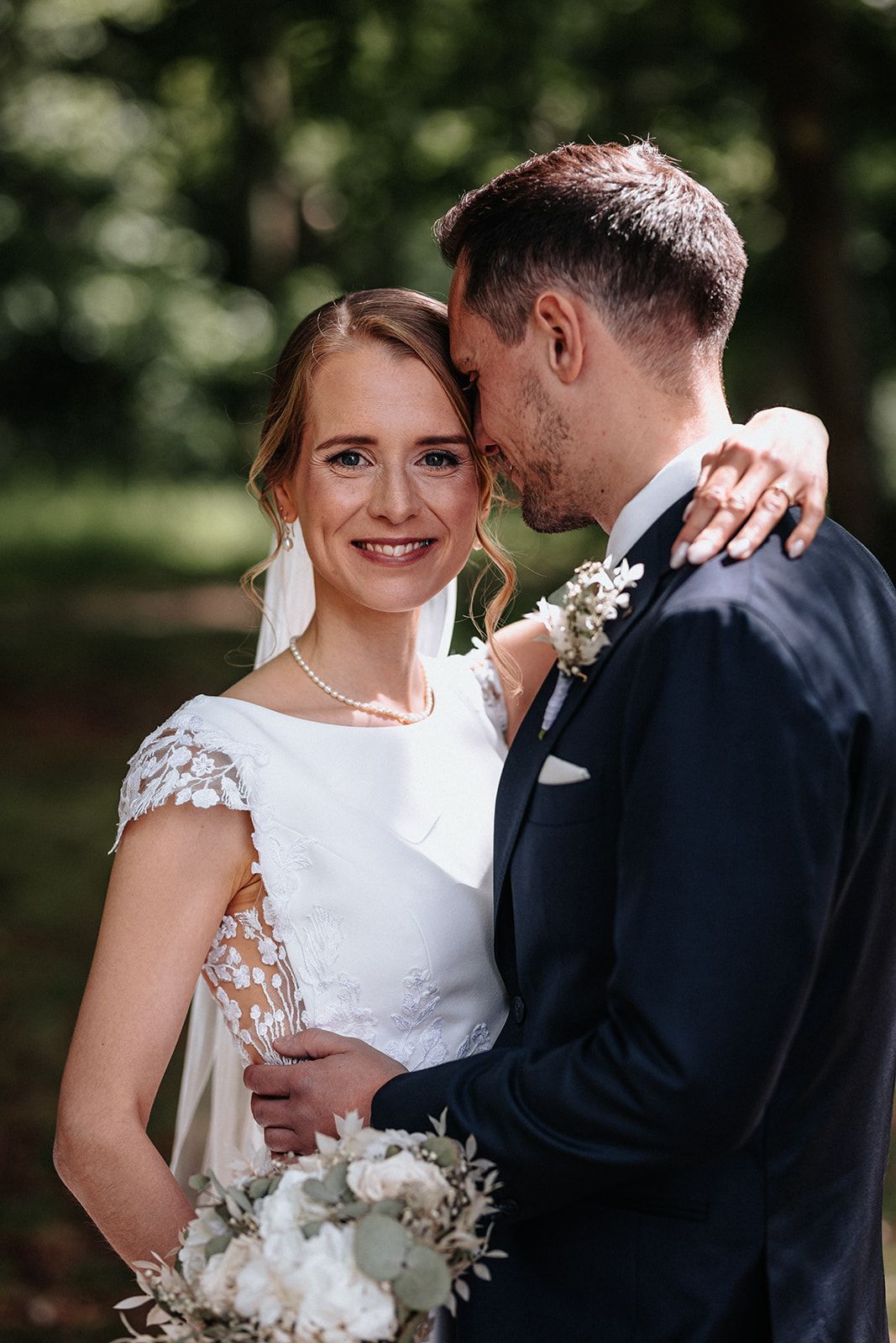 A bride and groom share intimate moments in a garden setting with white floral bouquet details.