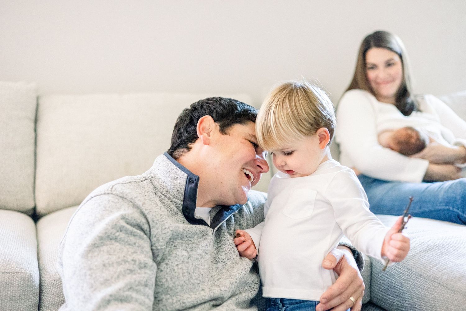 Family sharing joyful moment together while relaxing on gray couch at home. Aiken newborn photography