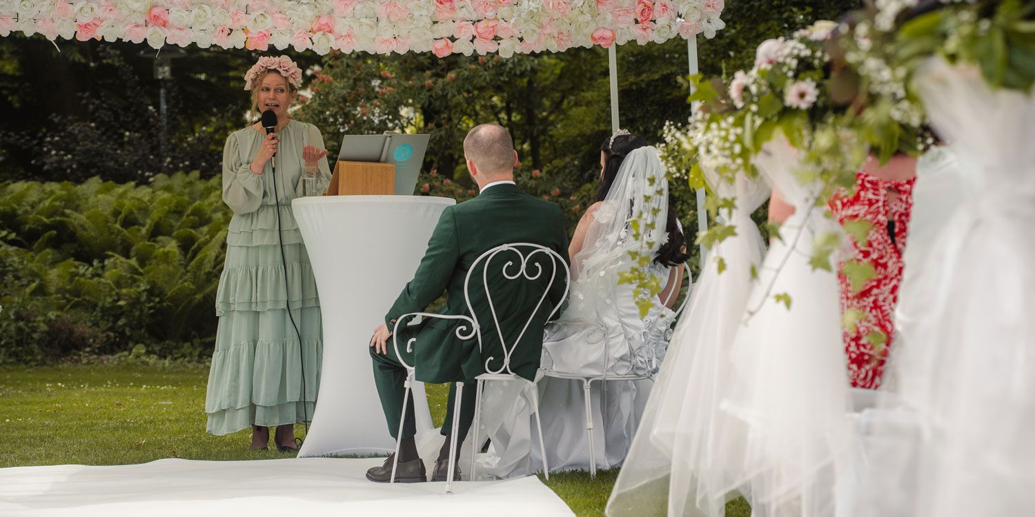 Ehepaar sitzend vor der Traurednerin mit Blumengesteck von Fingerschwur Hochzeiten