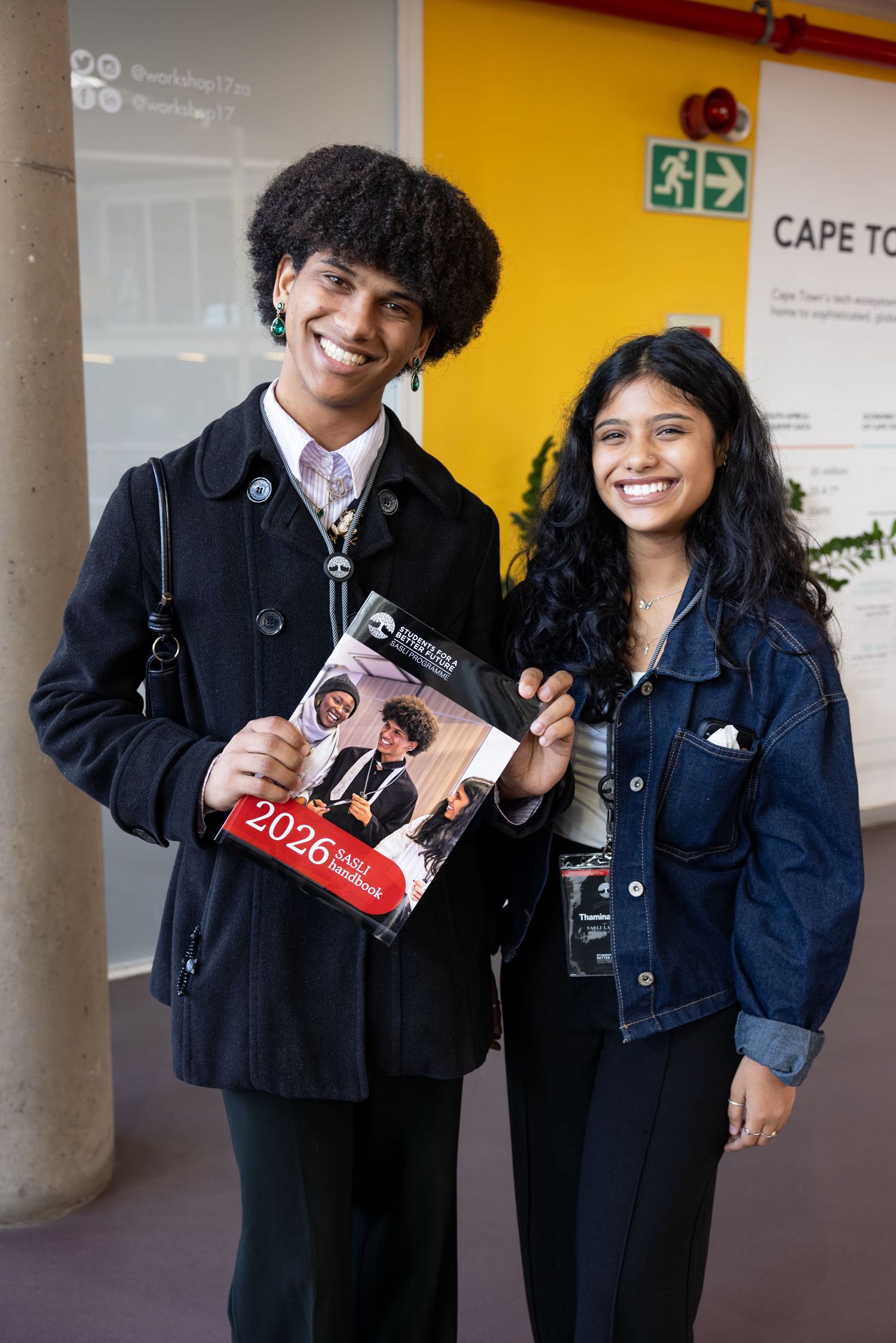 Two attendees pose with event materials at a conference venue with colorful walls.