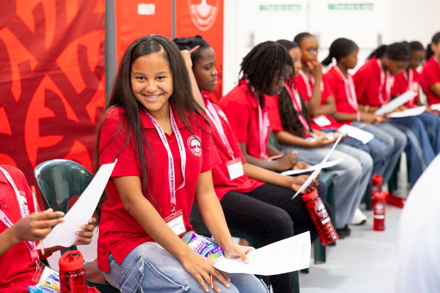 Students in red uniforms participate in an interactive learning session at tables.