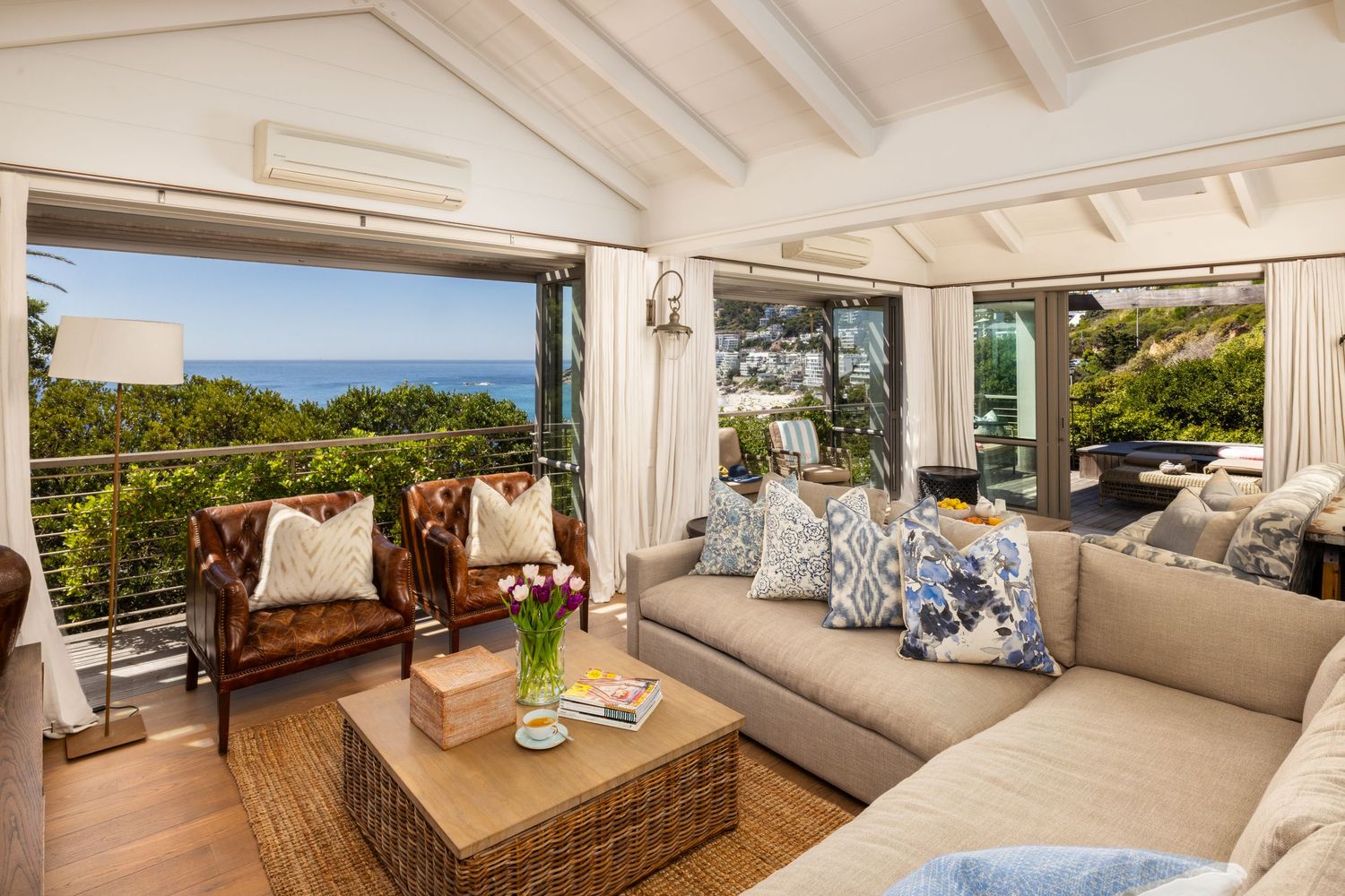 Modern coastal living room features panoramic ocean views through floor-to-ceiling windows and neutral furnishings.