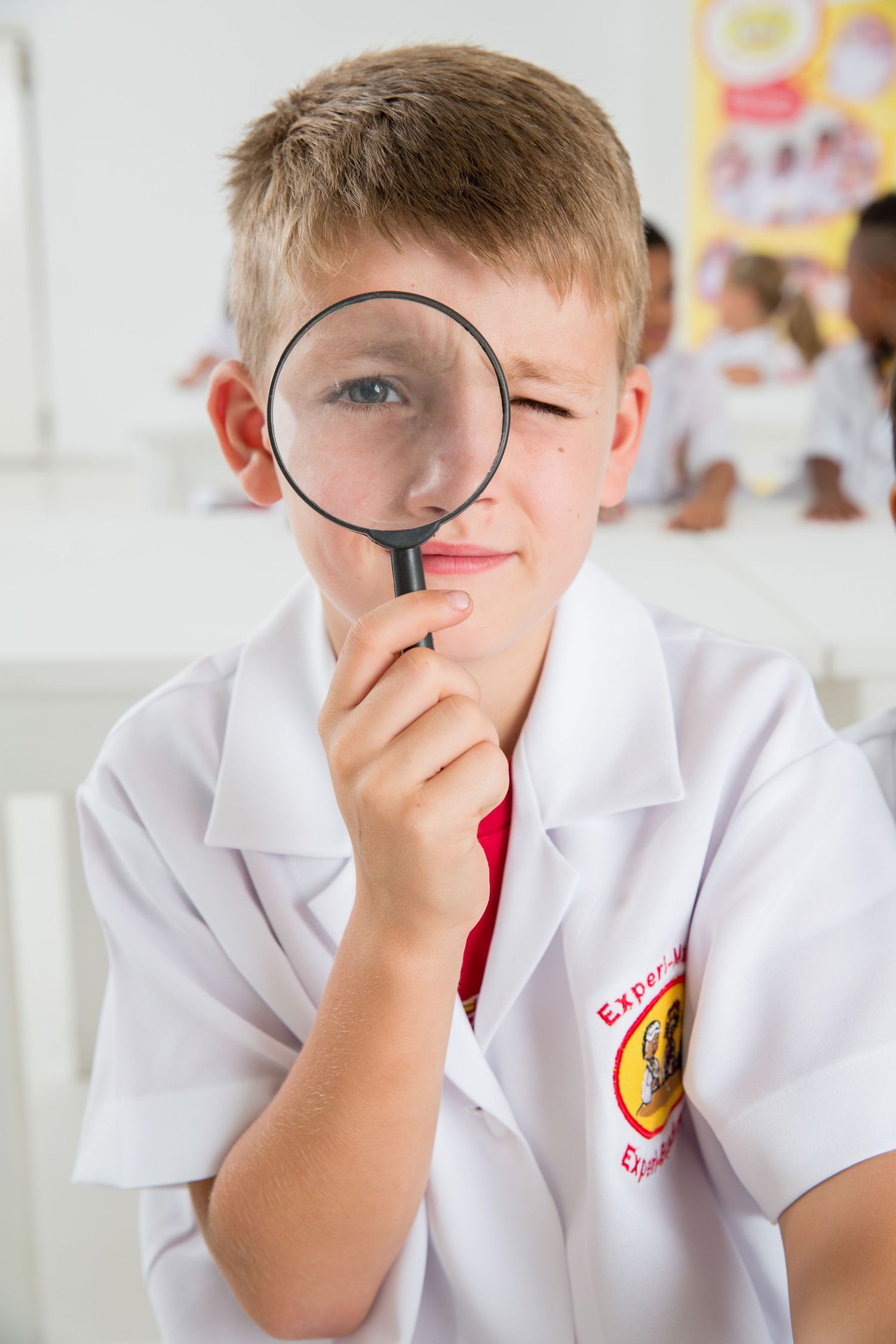 Student looks through magnifying glass while wearing white lab coat in science class.