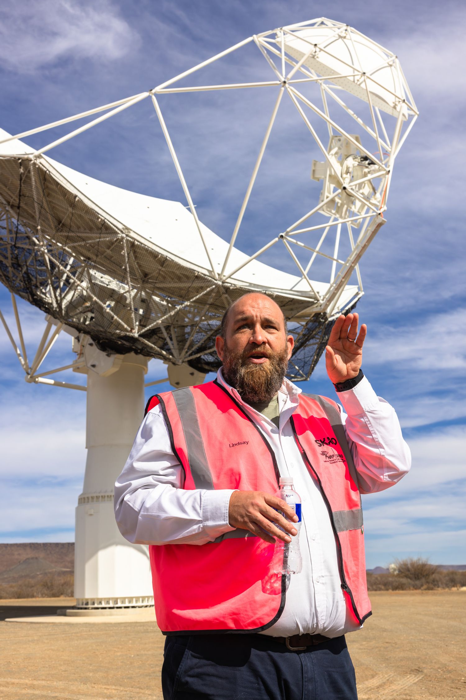 Guide in safety vest gesturing while explaining features of a large radio telescope dish.