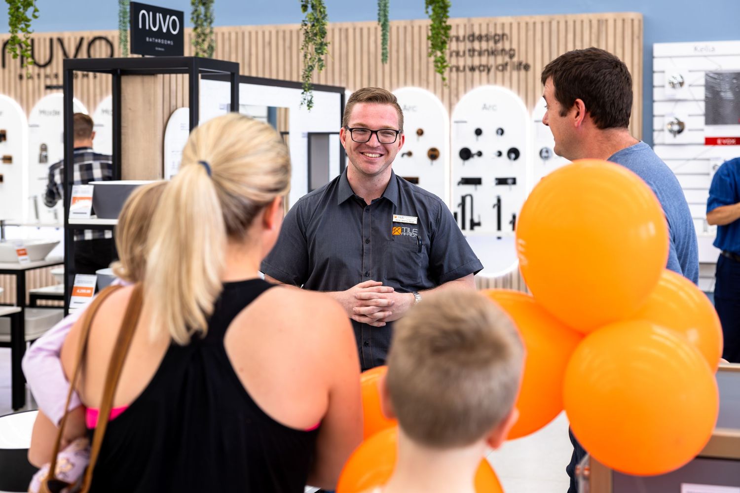 Retail employee greeting customers with orange balloons at store entrance.