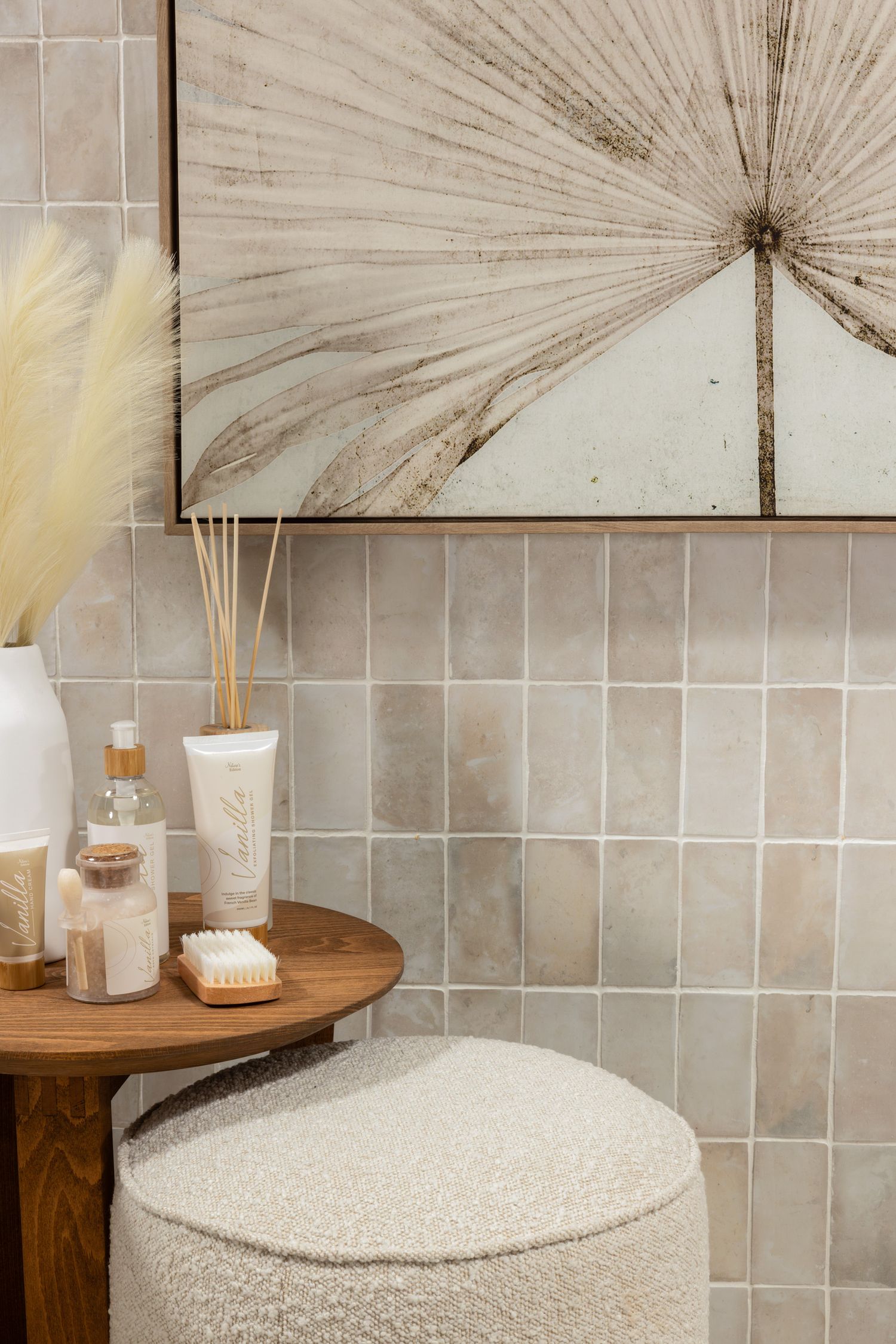 Serene bathroom corner with vintage fan artwork, grey tiles, and wooden stool displaying spa accessories.