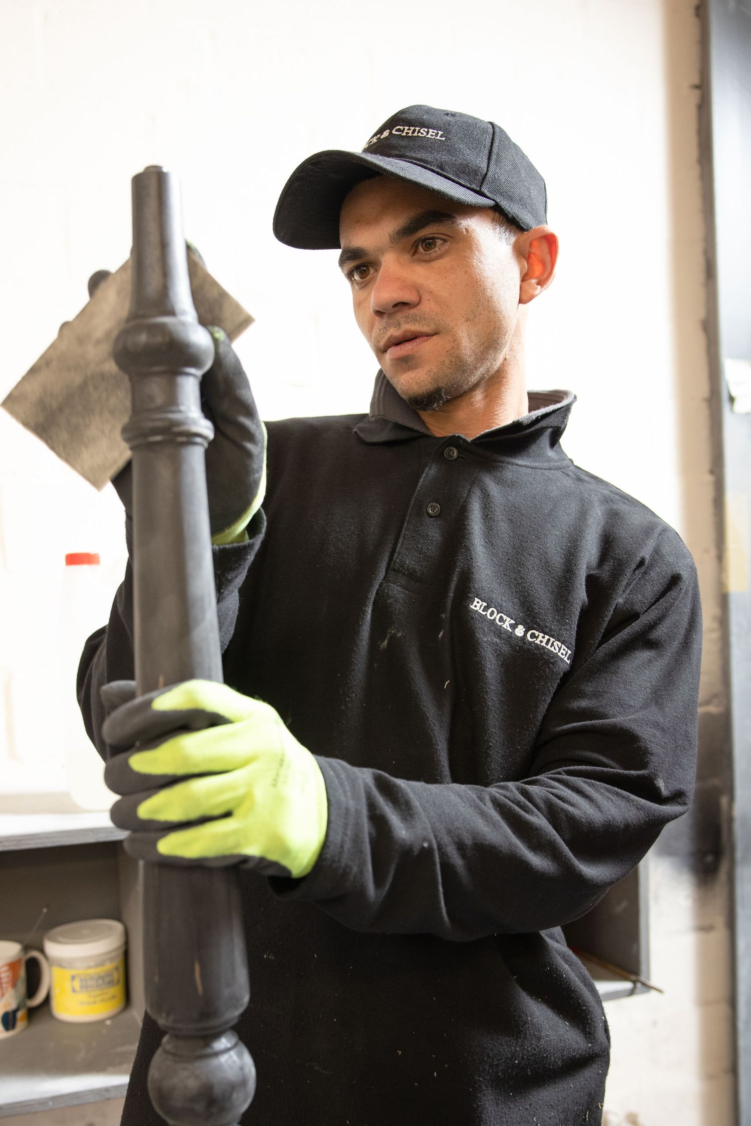 Worker in protective gear inspects black metal components in a factory setting.