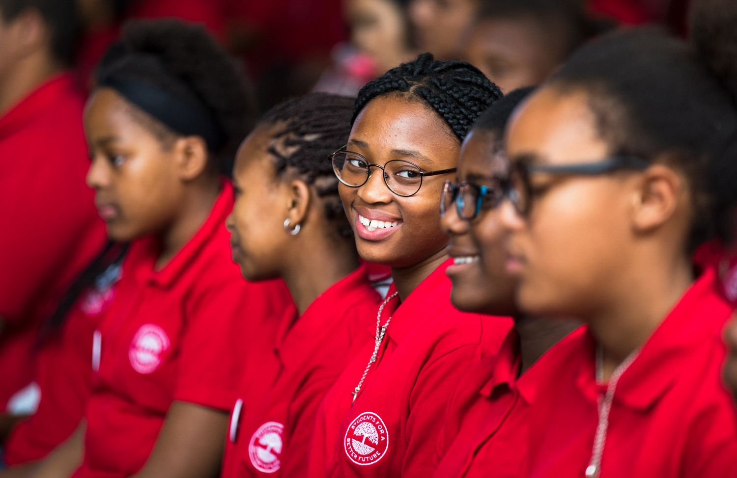 Students wearing matching red uniforms sit together in an assembly.