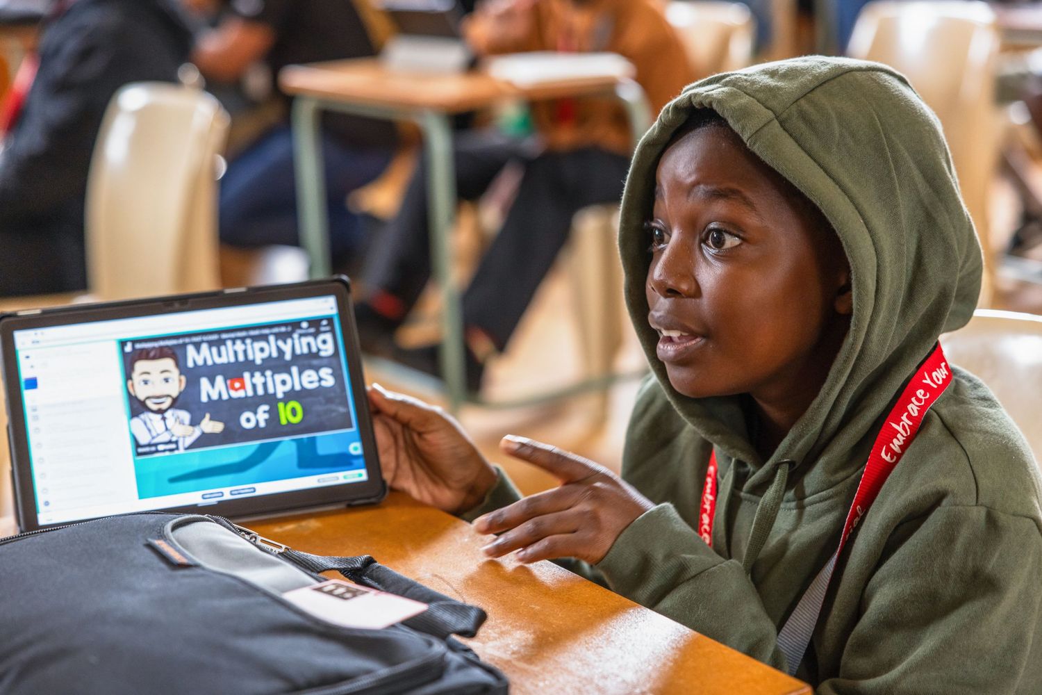 Student in green hoodie works intently on laptop during technology education workshop.