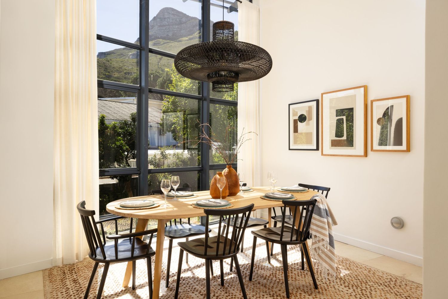 Modern dining room with round wooden table, black chairs, pendant light and framed artwork on white walls.