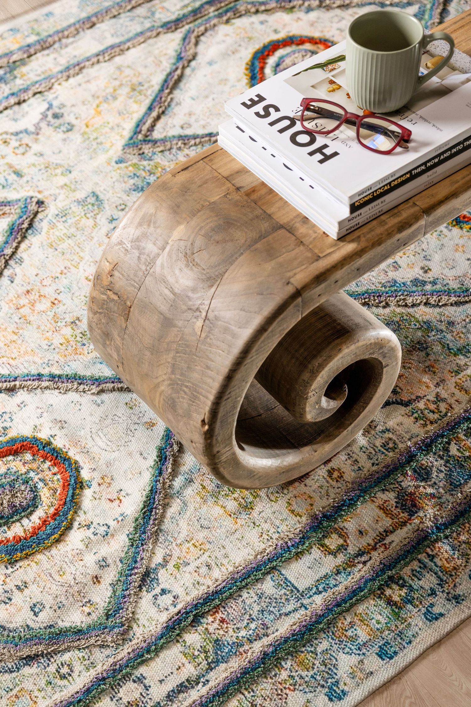 Modern styled room featuring a curved wooden accent piece and books on a decorative area rug.