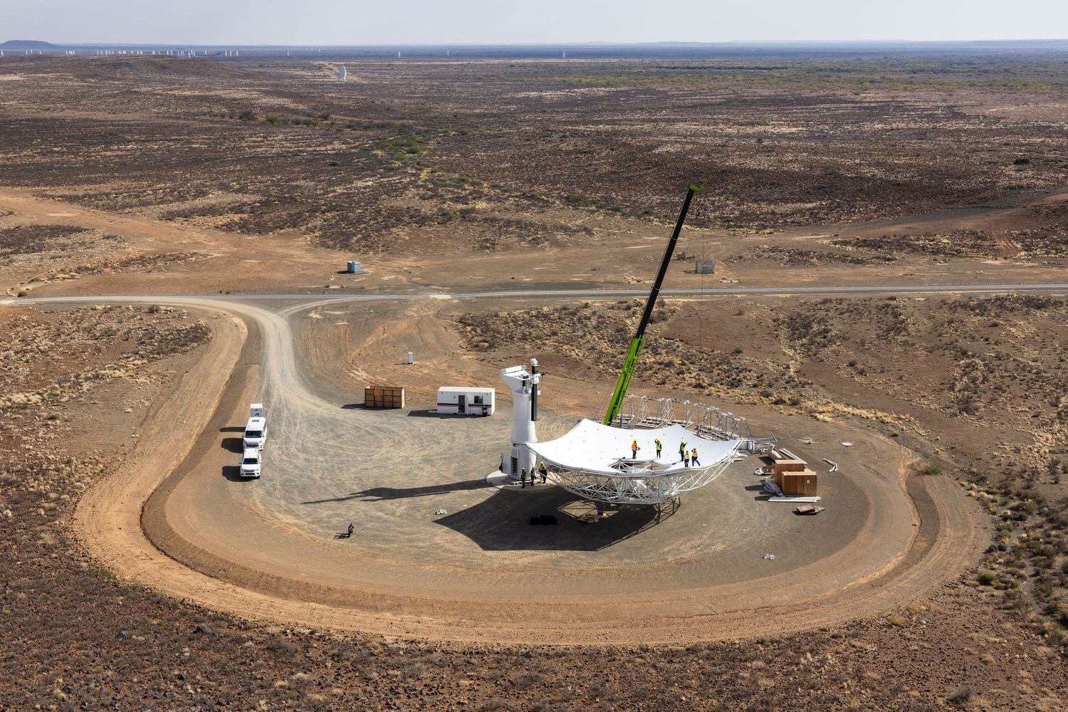 An aerial view of a circular dirt road leading to a satellite dish installation in a remote desert location.