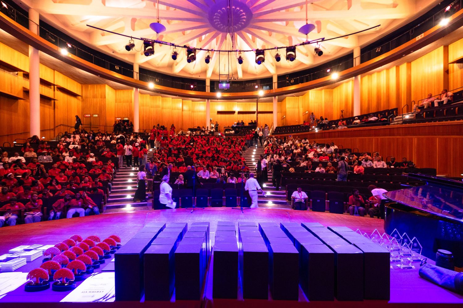 Large auditorium with dramatic orange and purple lighting illuminating the ceiling and stage area.