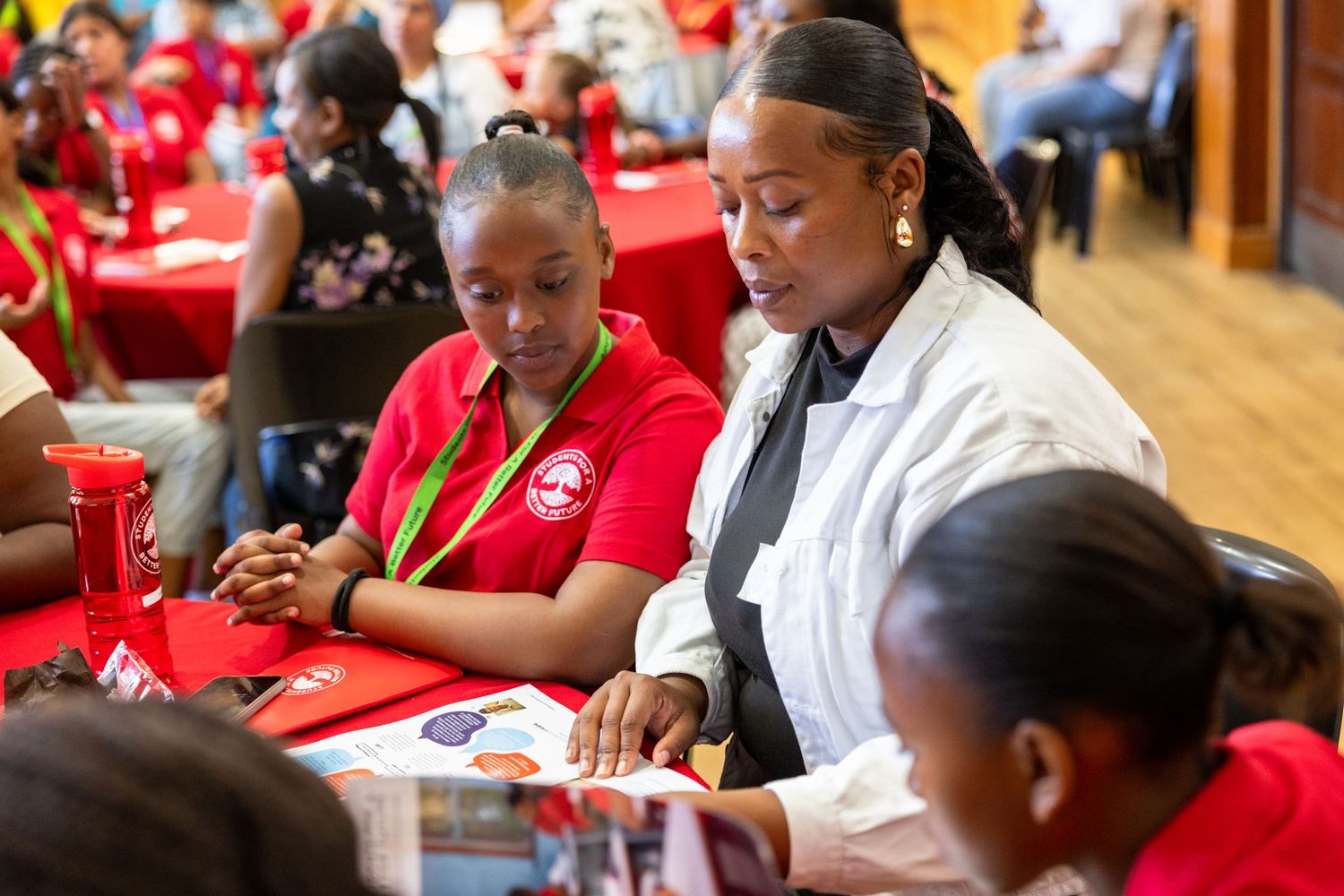 Students engage in discussion at tables with red tablecloths during an educational event.