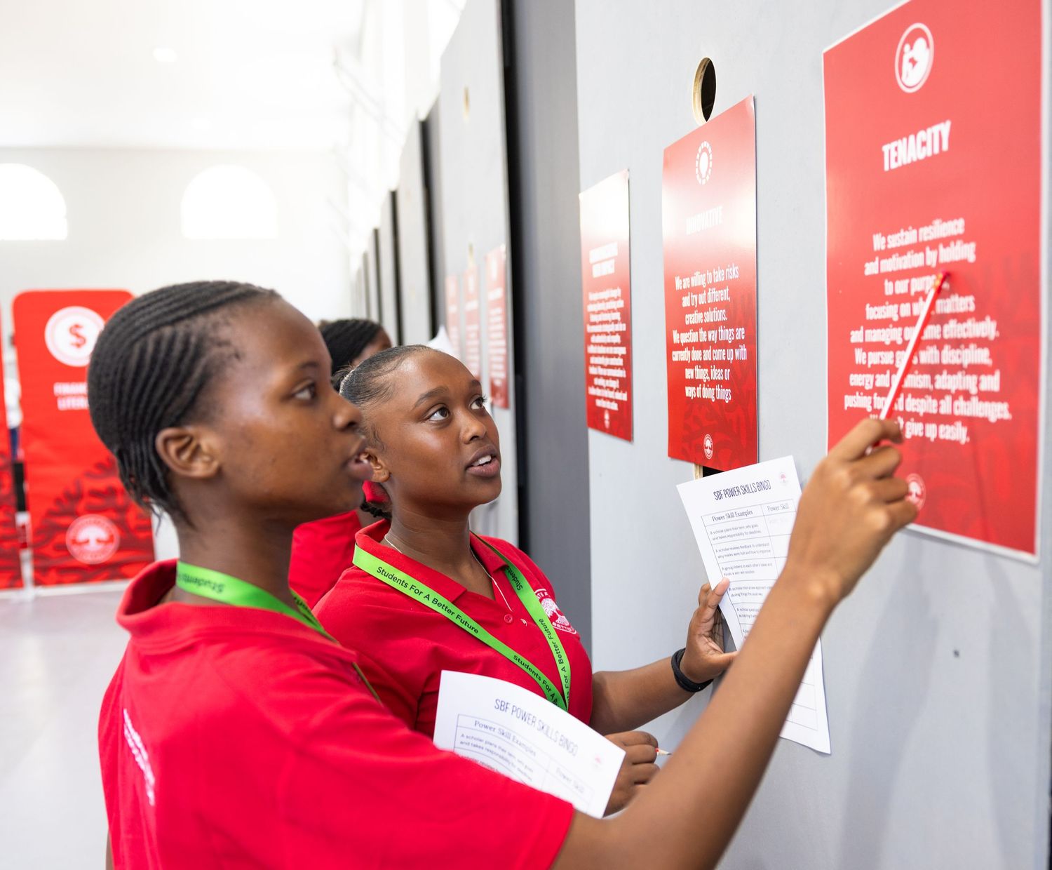 People in red shirts read and interact with information posted on a wall display.