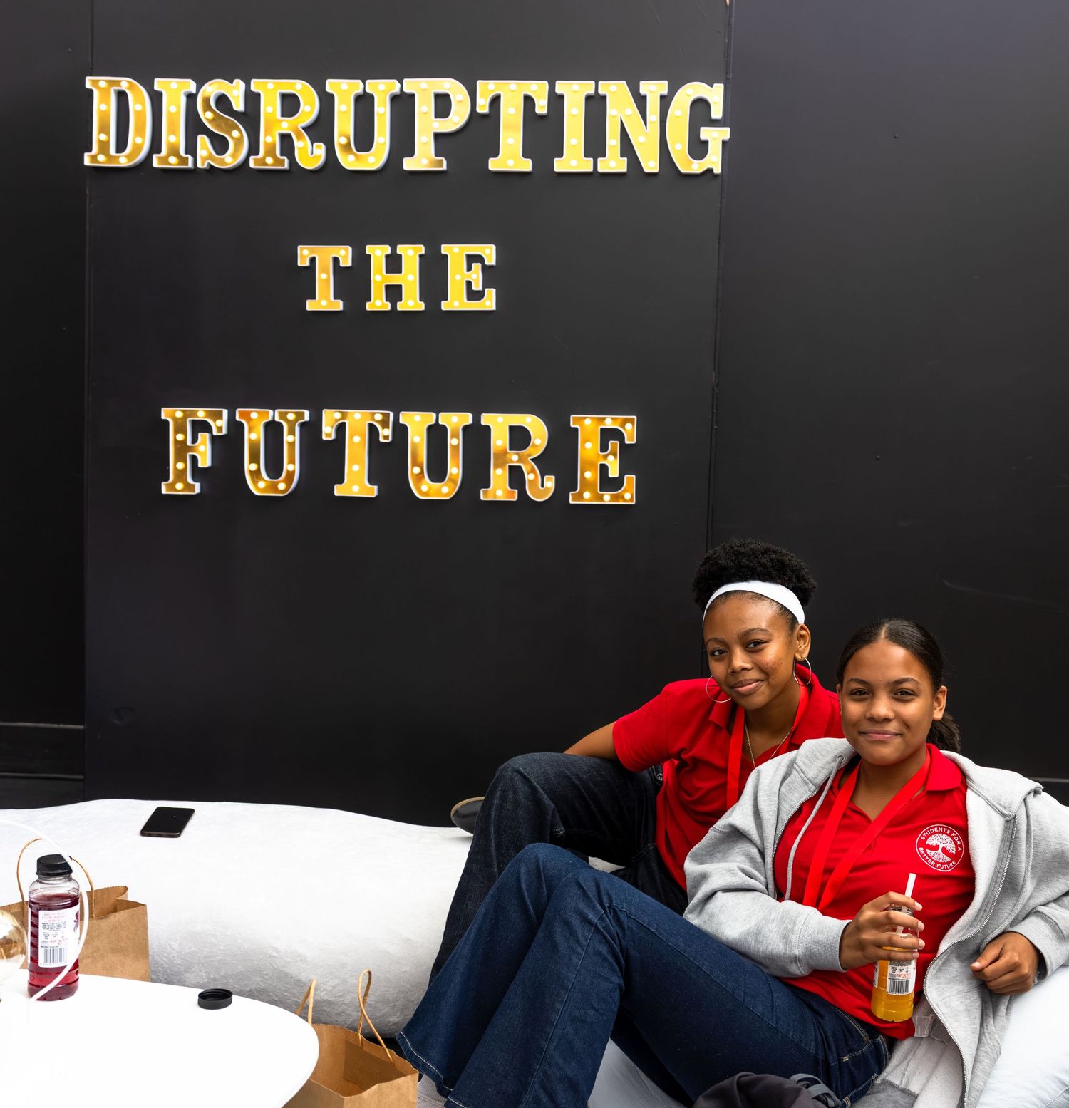 Two people relax on a couch beneath text reading 'Disrupting the Future' in gold letters on a black wall.