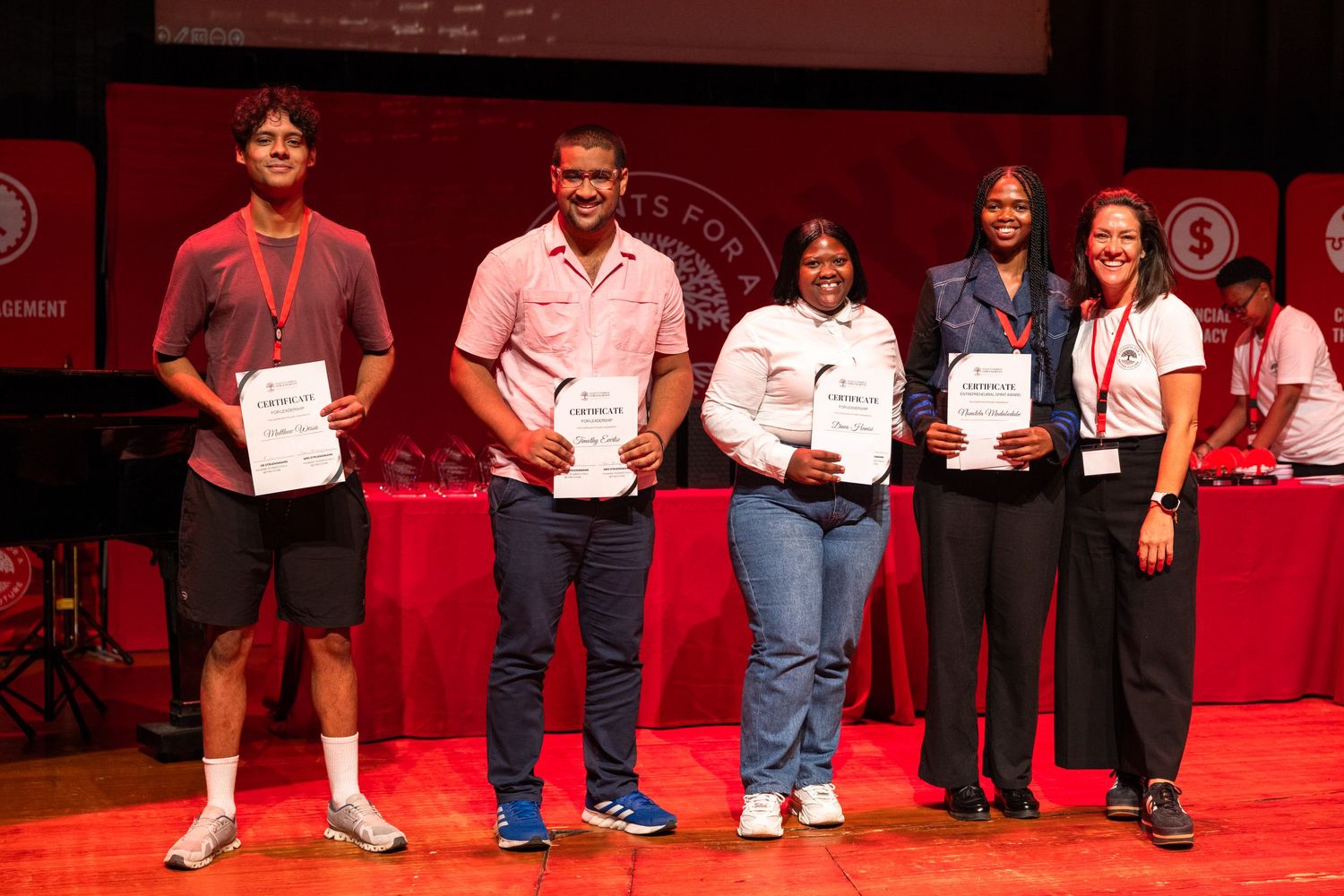 A group of people in red shirts standing together for a group photo on stage.