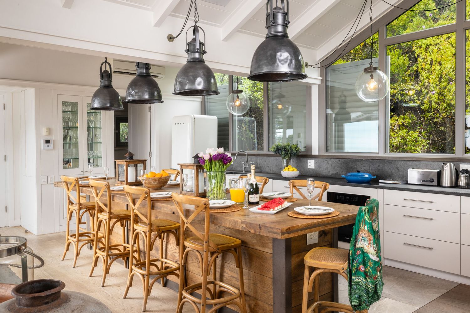 Modern open-concept kitchen and dining area with wooden bar stools and pendant lighting overlooking ocean views.